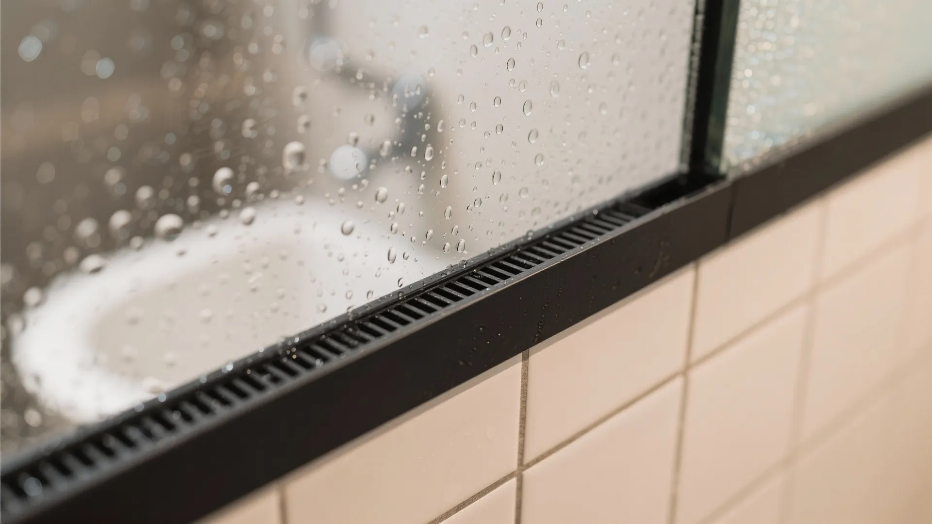 Close up view of water droplets on a glass shower door with black floor drain detail