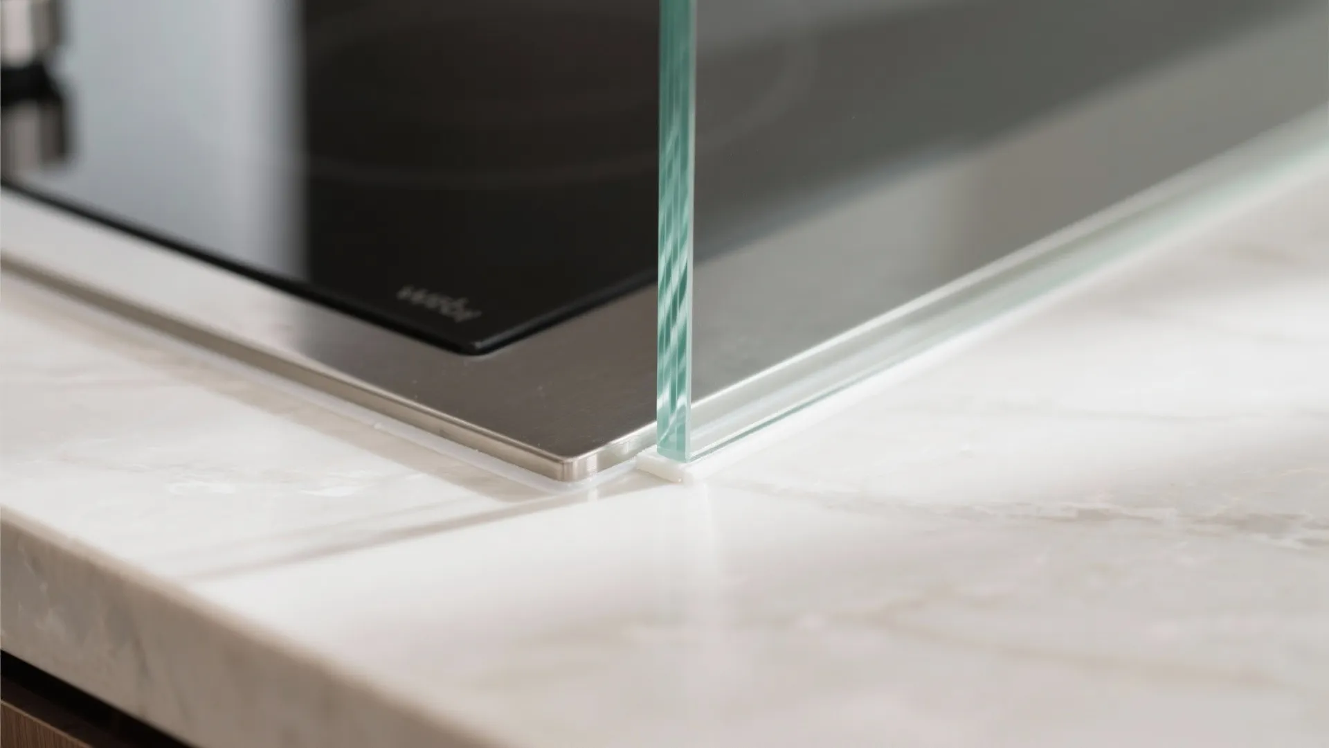 Close up of glass partition edge installed on marble countertop near black electric stove top