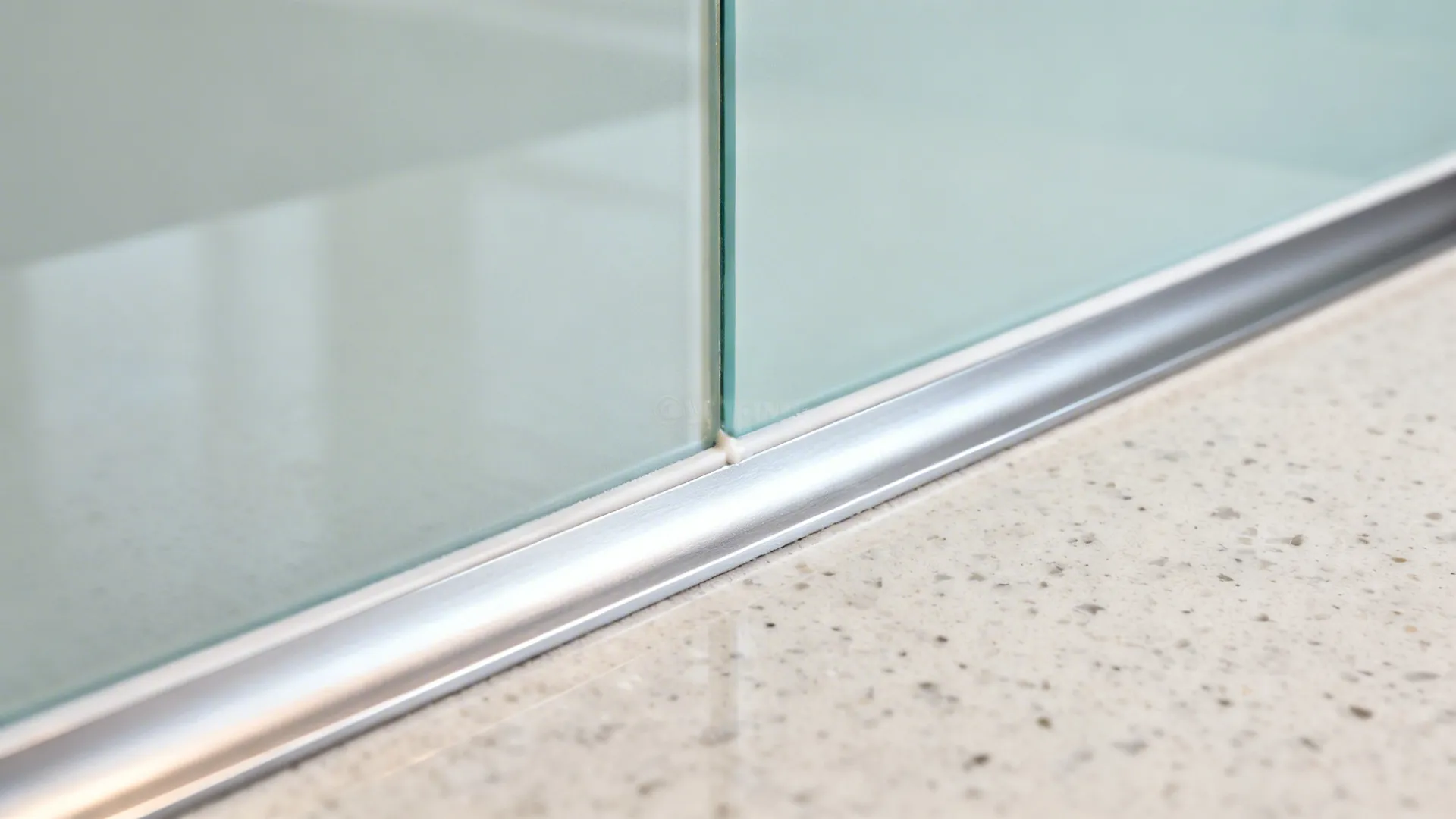 Macro of back-painted glass backsplash edge with neat silicone and trim above quartz.