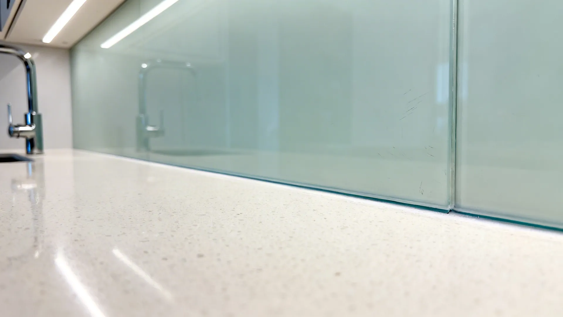 Close up detail of a white stone kitchen countertop meeting a green glass wall panel