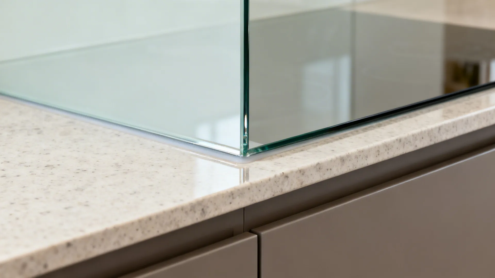 Macro of toughened glass backsplash edge with silicone joint above quartz top.
