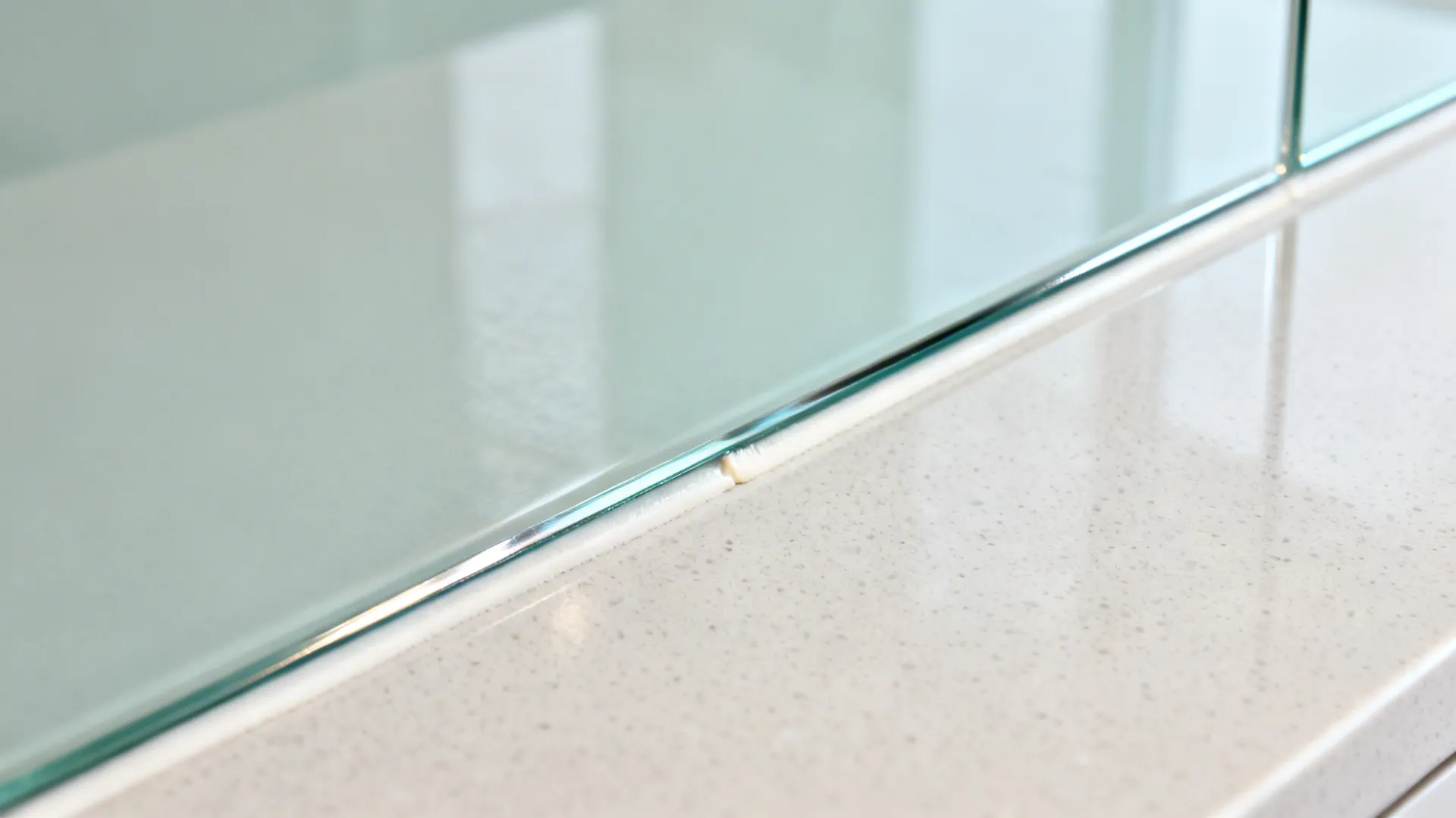 Macro of polished low-iron glass backsplash edge meeting a honed porcelain countertop.