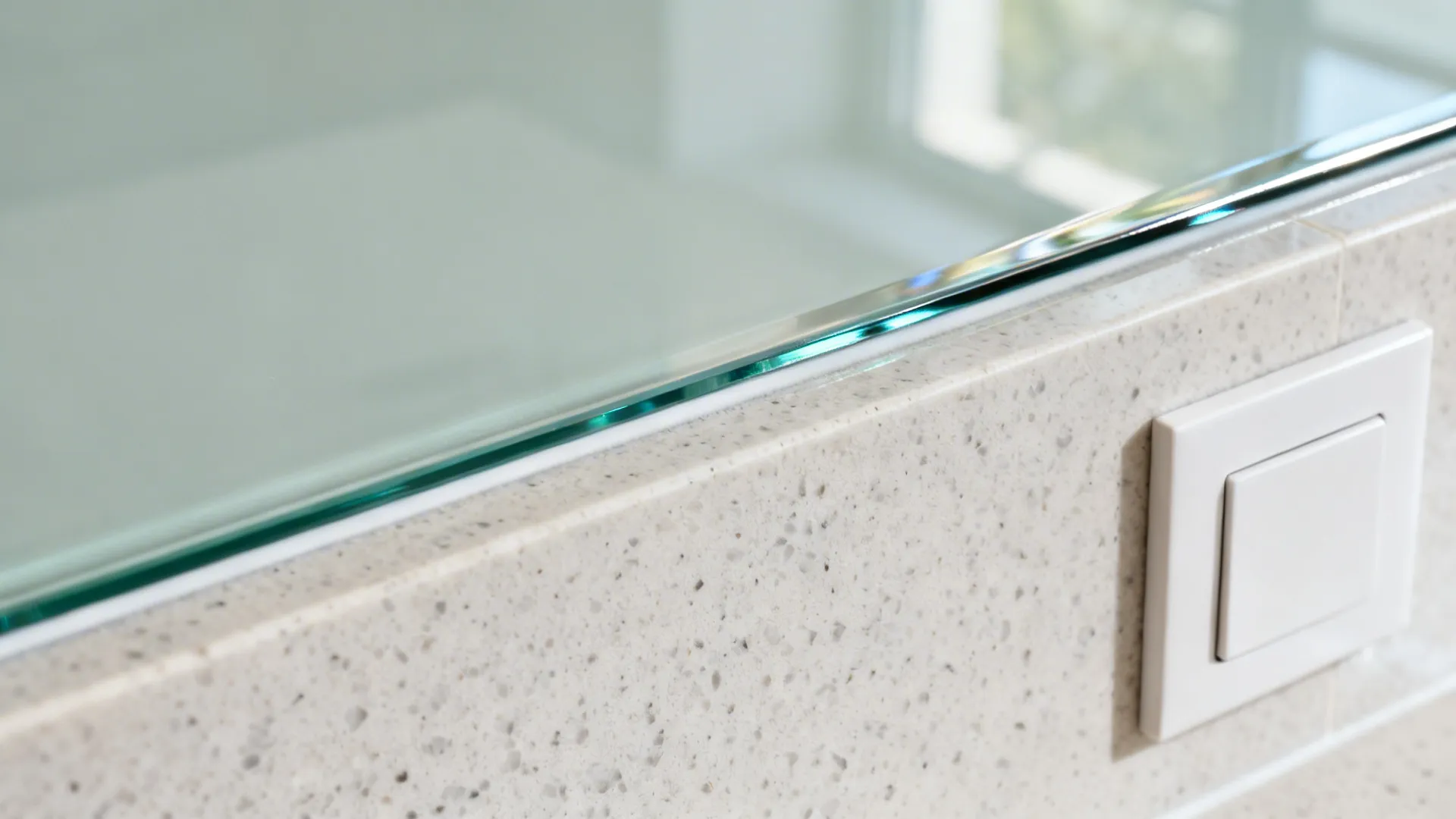 Macro of low-iron glass backsplash edge reveal above quartz with aligned outlet.