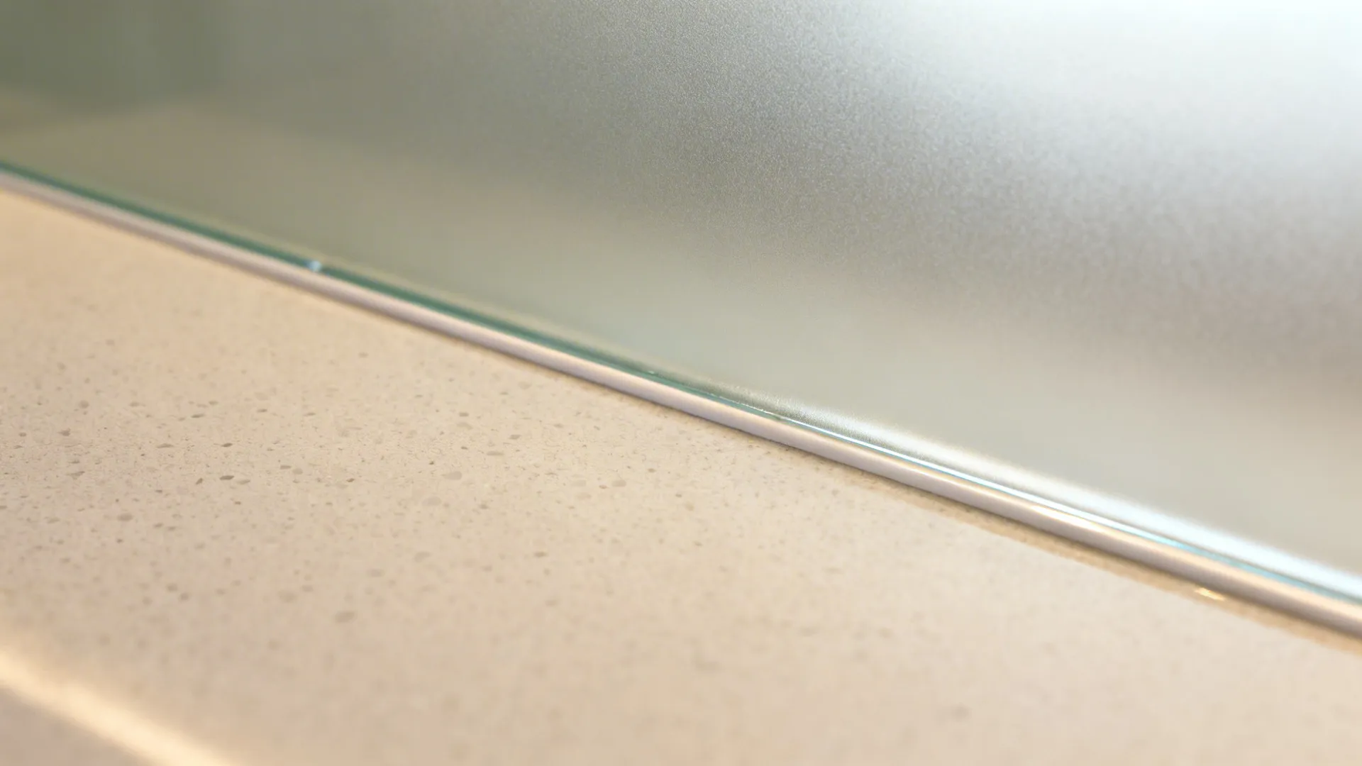 Macro of a polished matte glass backsplash edge meeting a pale quartz countertop in soft daylight.
