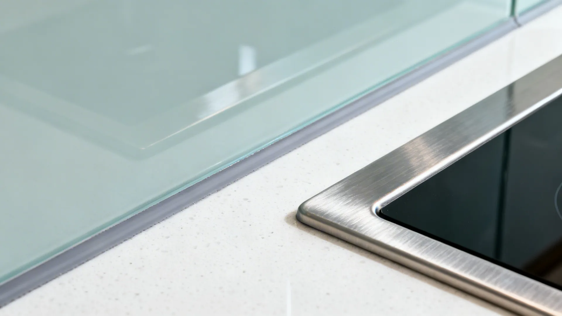 Close-up of gray back-painted glass meeting quartz with a stainless insert panel.