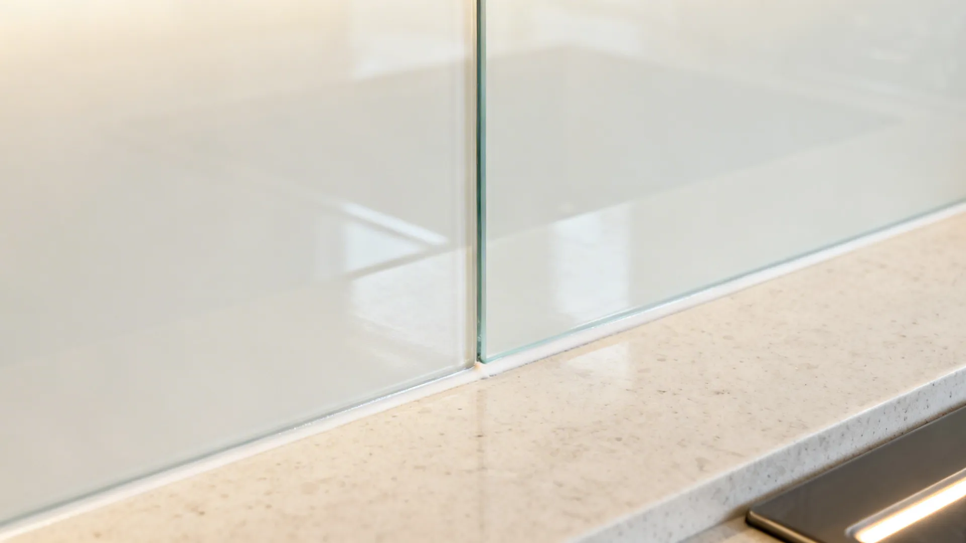 Close up of glass panel edge installed on a white stone kitchen counter with waterproof sealant