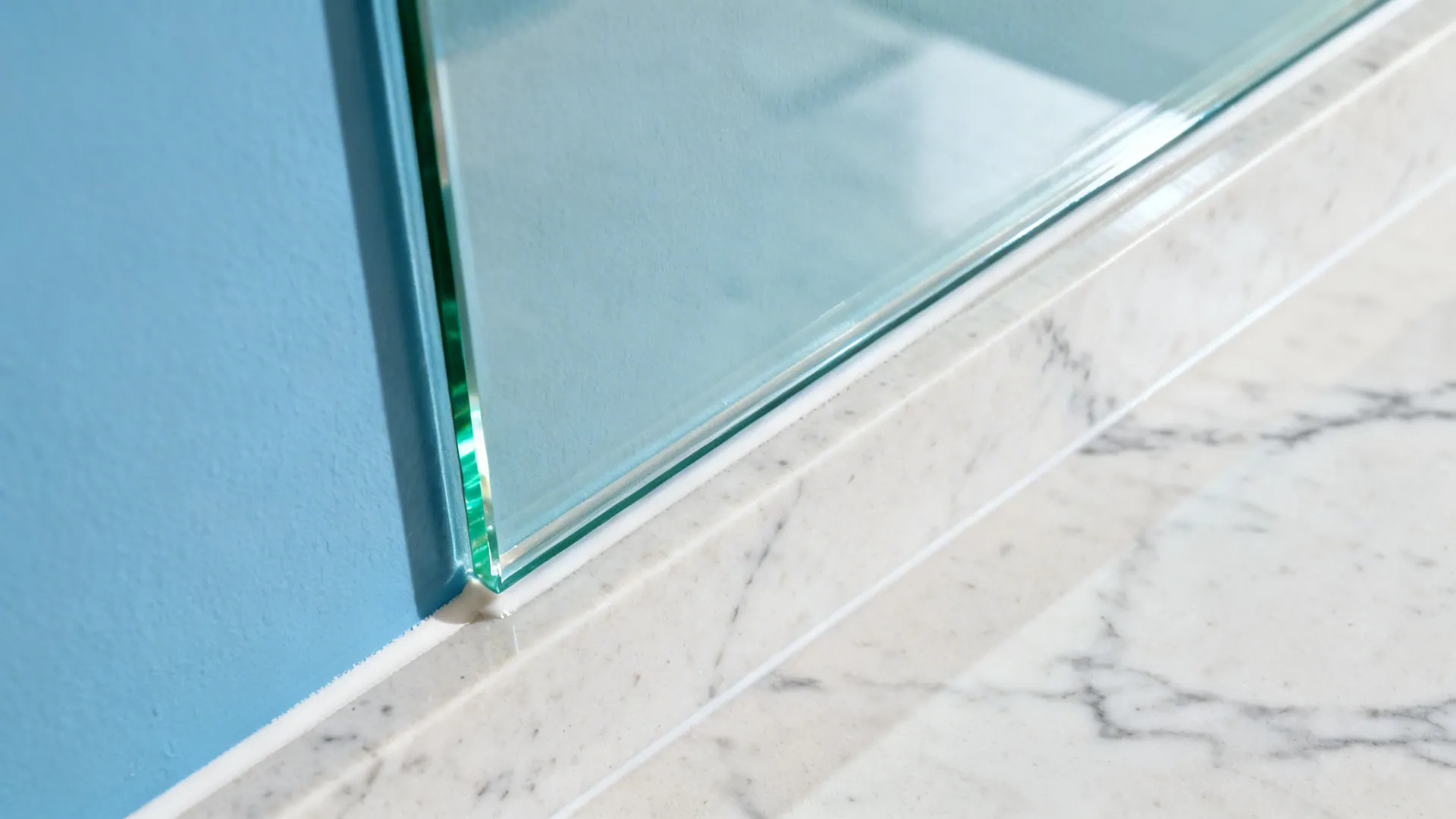 Macro view of low-iron glass backsplash edge over sky-blue paint with clean seam.