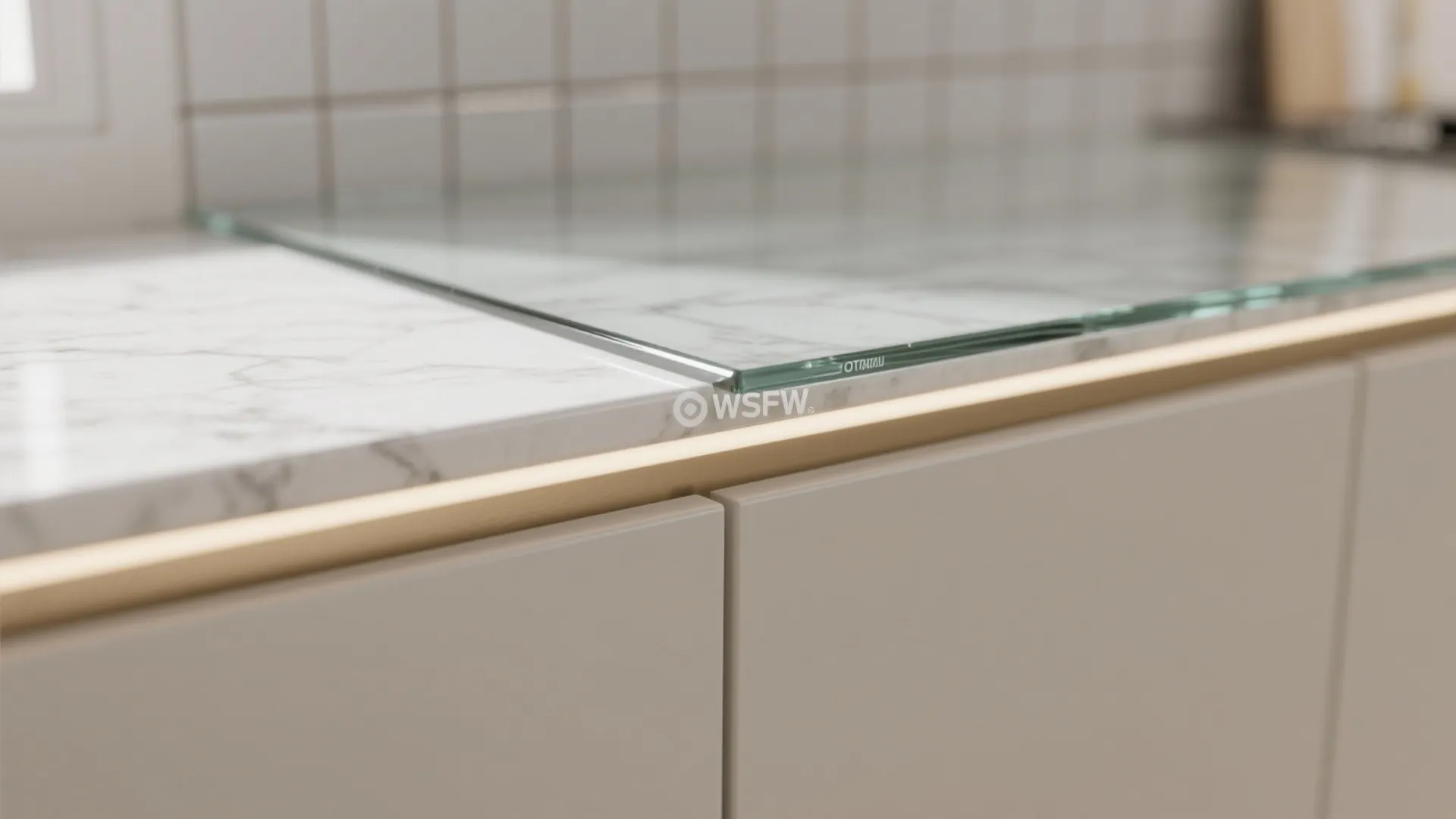 Close up of glass panel resting on white marble countertop with light strip and grey cabinets