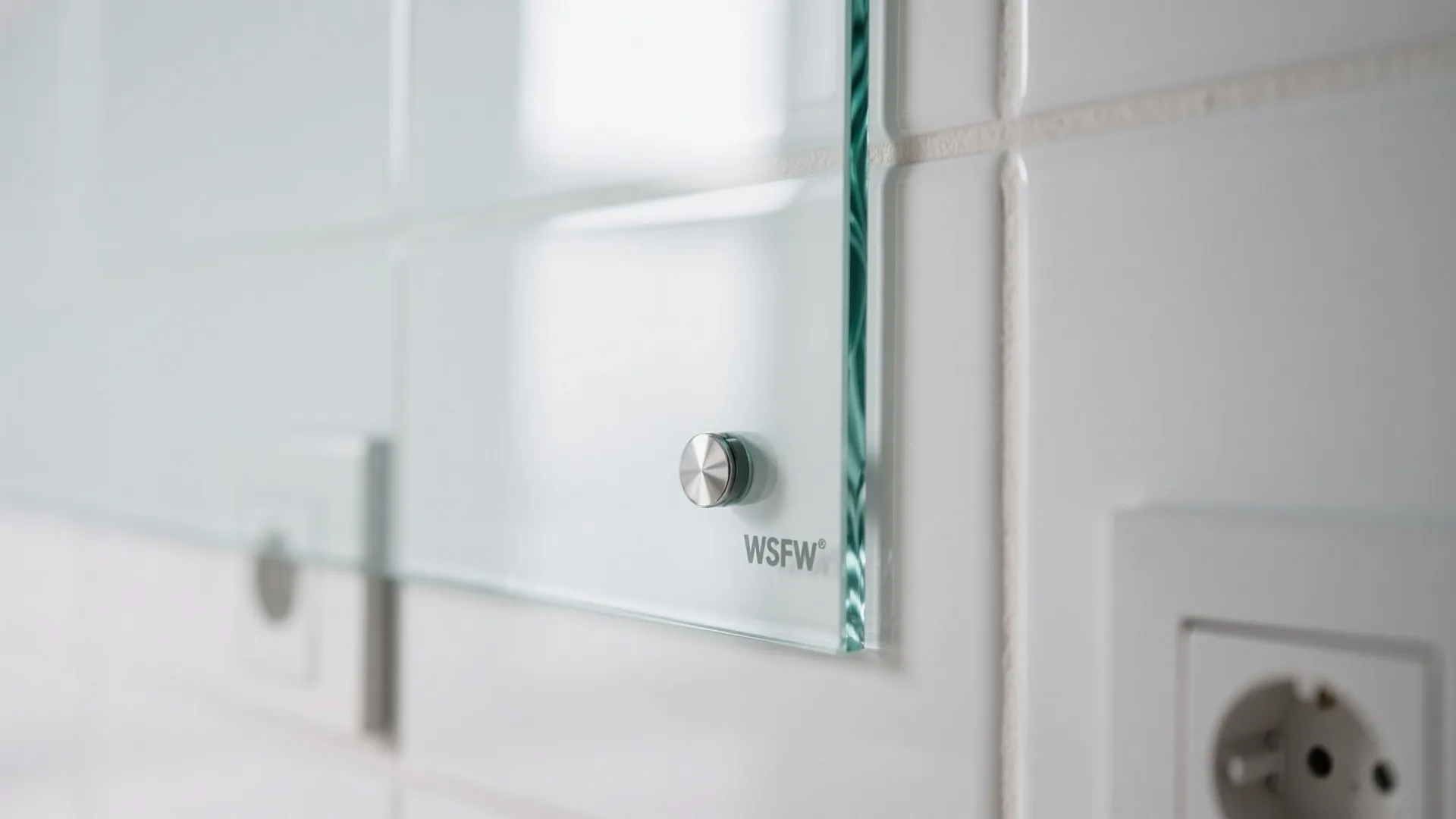 Close up glass panel with metal fastener mounted on white tiled wall with electrical outlet