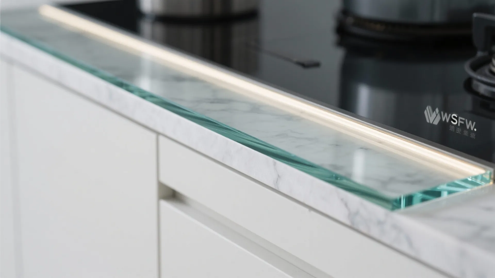 Close-up of low-iron glass backsplash edge with quartz counter and silicone seam.