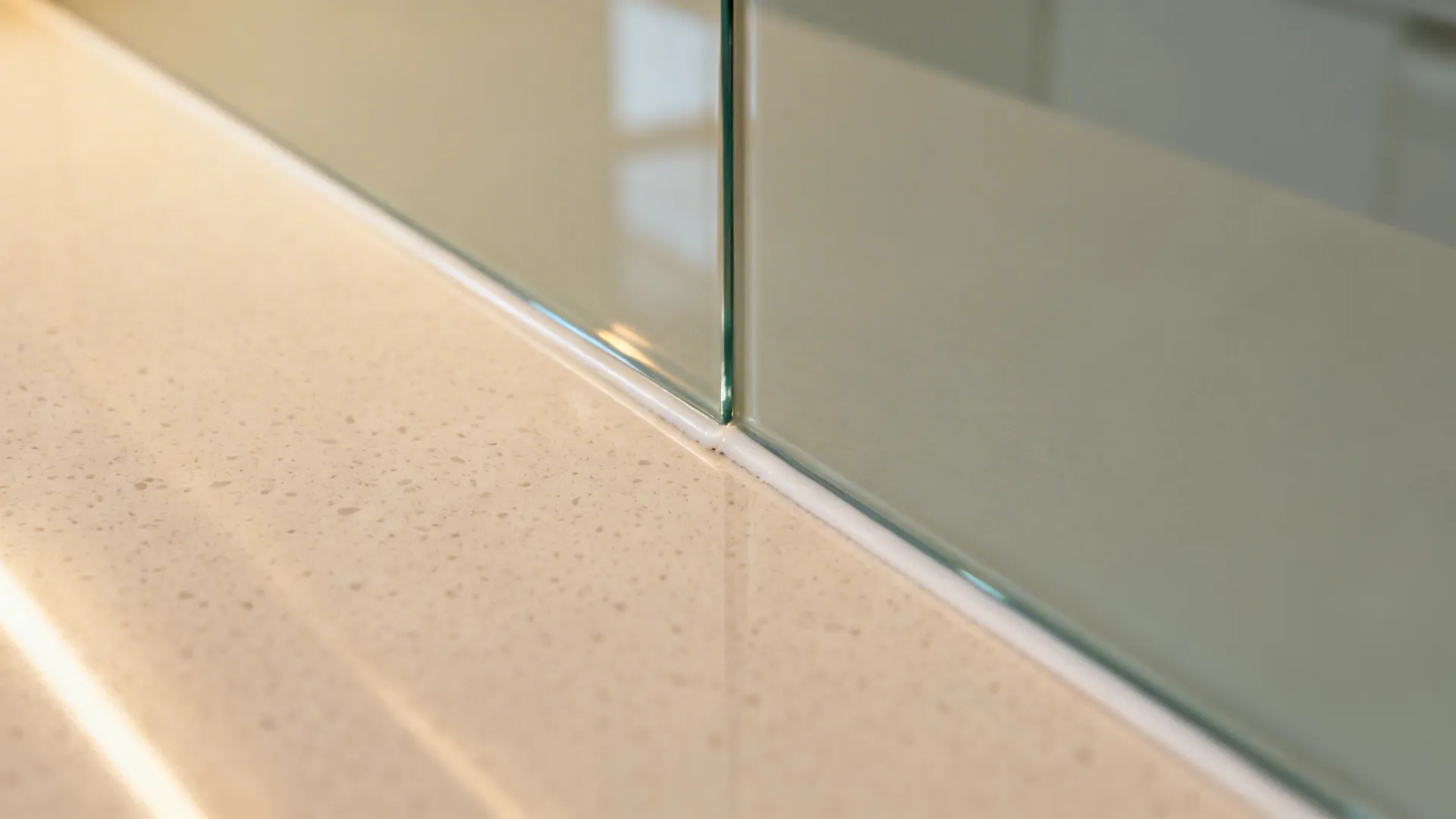 Close up view of glass panel meeting stone countertop with white sealant in modern kitchen