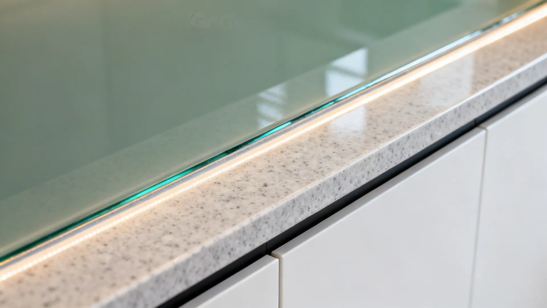 Close up of glass panel edge with integrated light strip on a white stone kitchen countertop