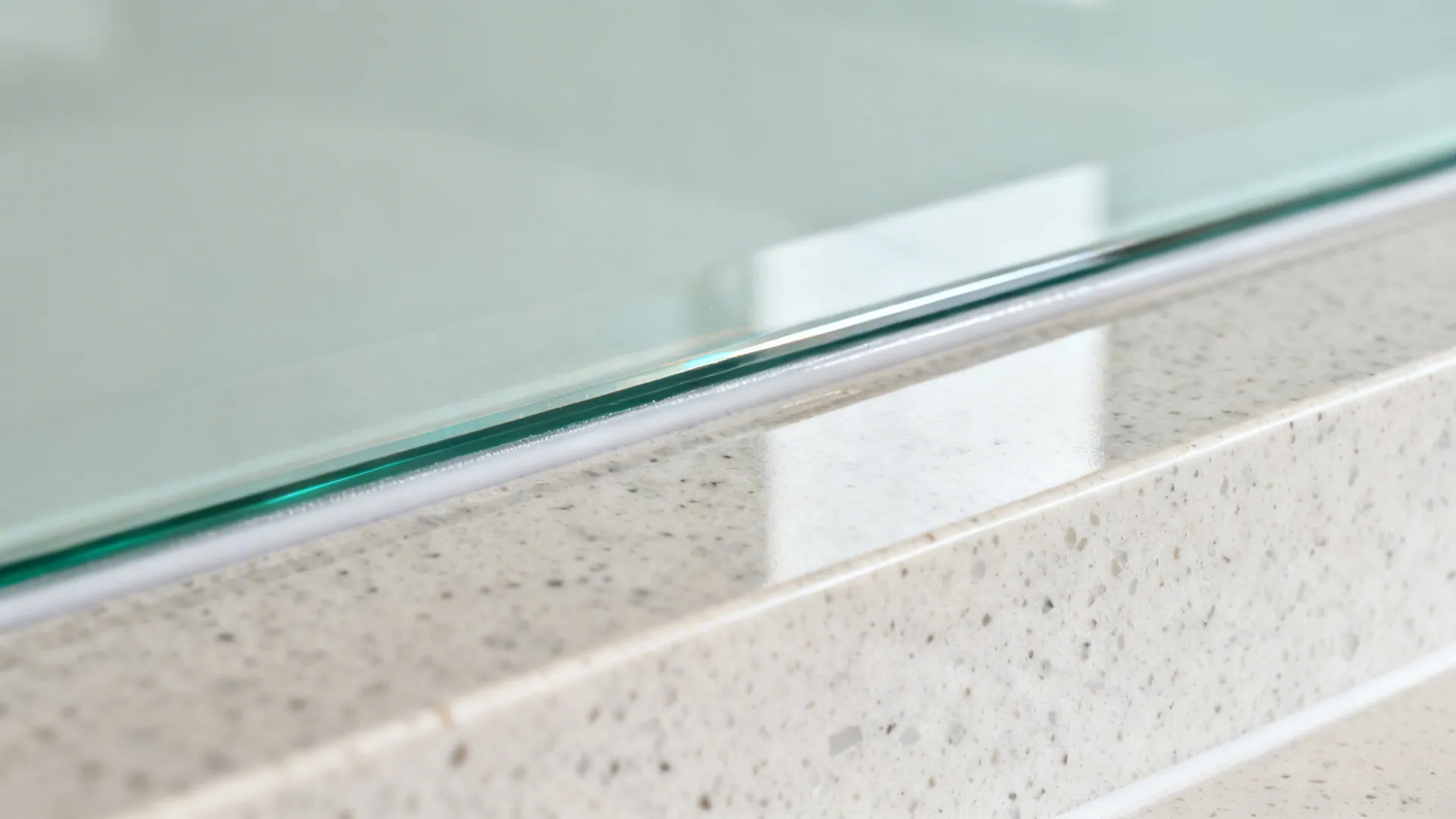 Macro view of a tempered glass backsplash edge with clean silicone joint over a quartz-look counter.
