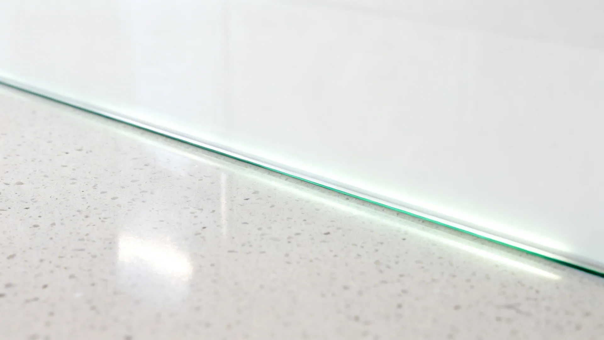 Macro of low-iron glass backsplash over quartz with clean silicone joint and soft LED reflections.