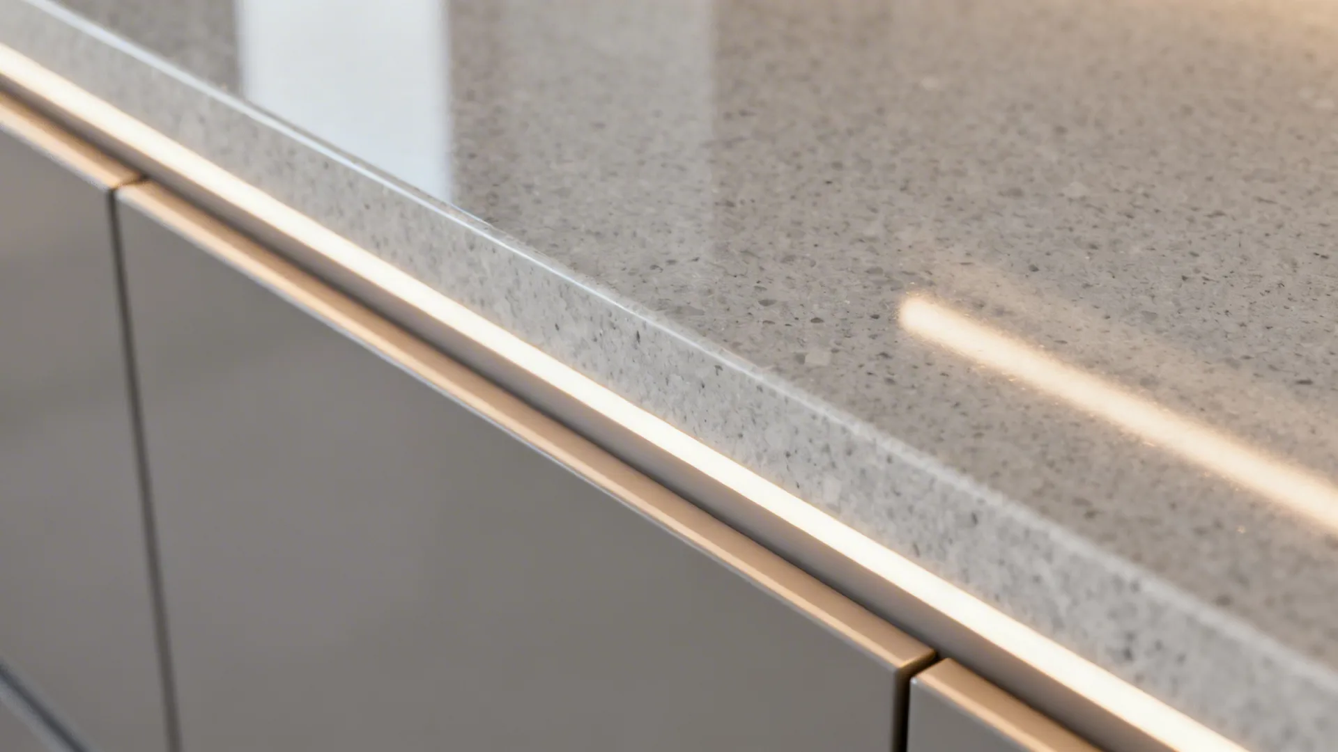 Macro of a warm gray back-painted glass backsplash meeting a quartz countertop.