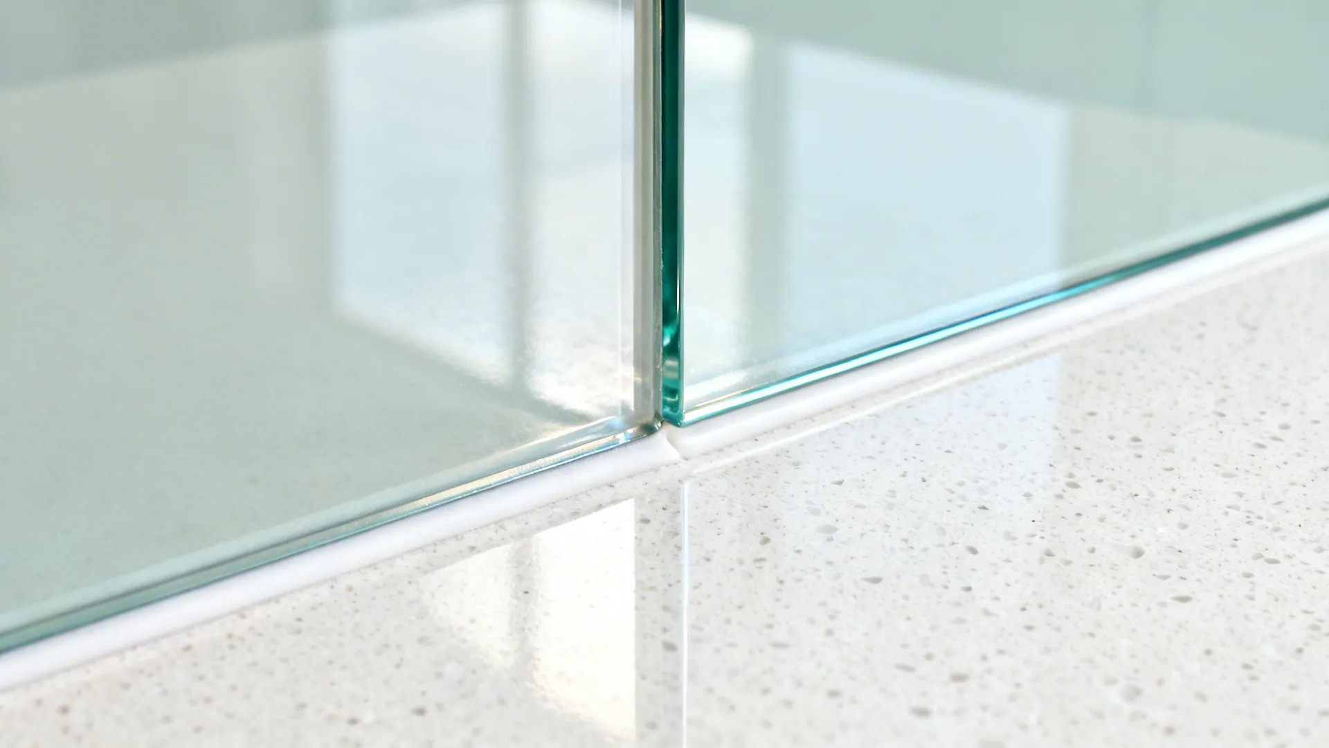 Macro detail of a back-painted glass backsplash meeting a quartz countertop.