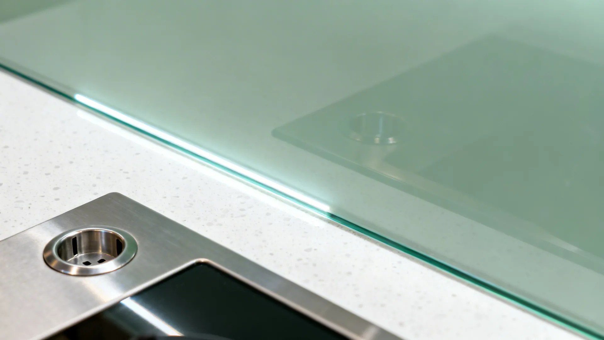 Macro of sage glass splashback with polished edge above white quartz worktop.