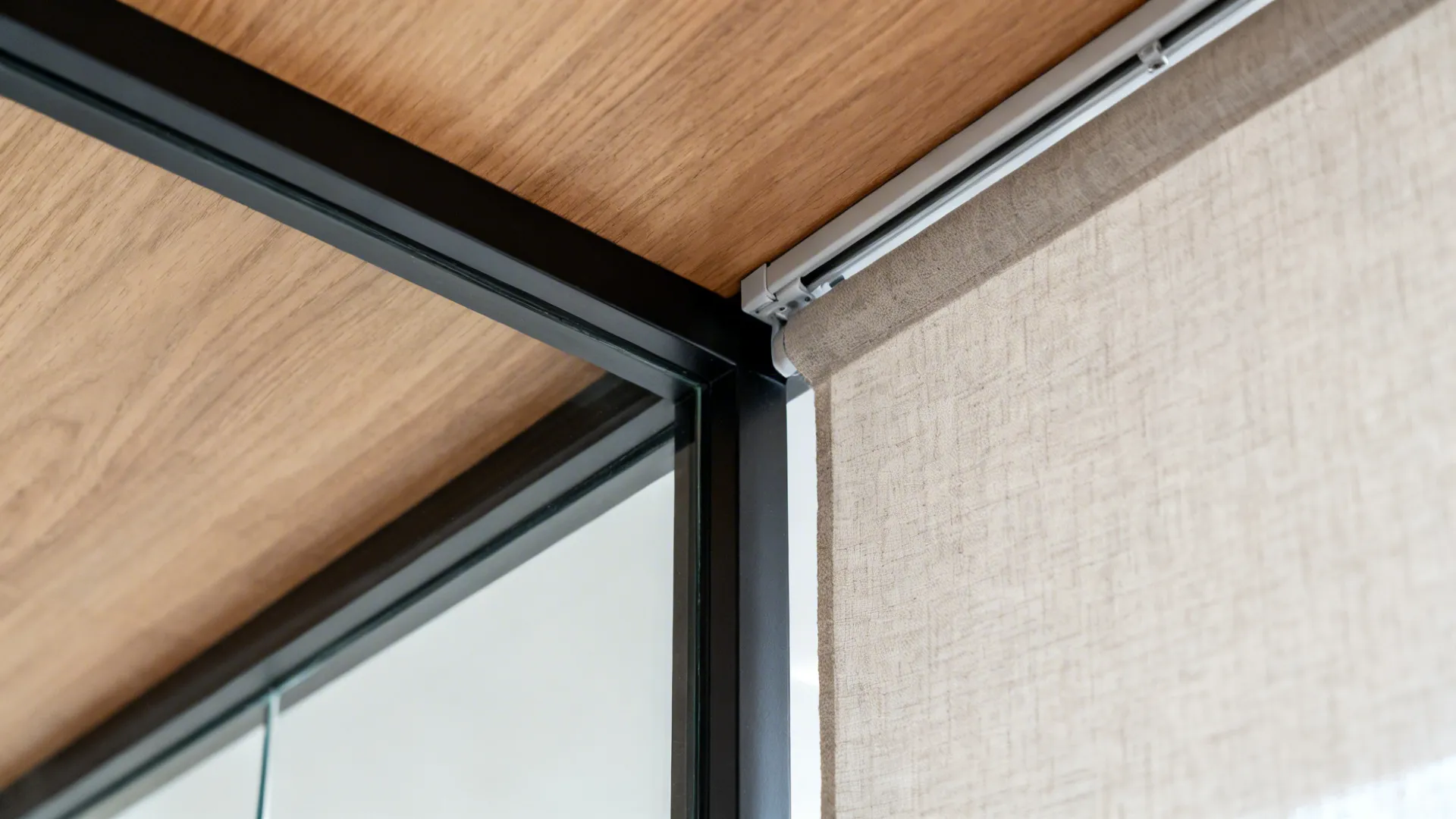 Macro detail of slim black steel-framed tempered glass partition with linen curtain track.