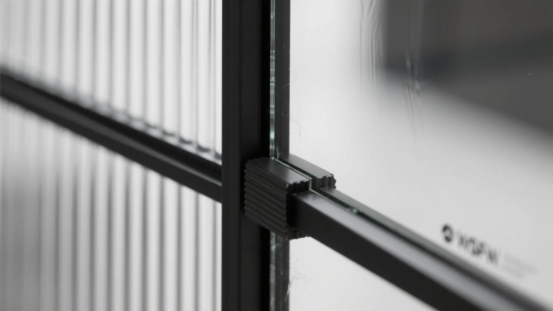 Macro of reeded glass panel meeting matte black steel frame with soft daylight diffusing through.