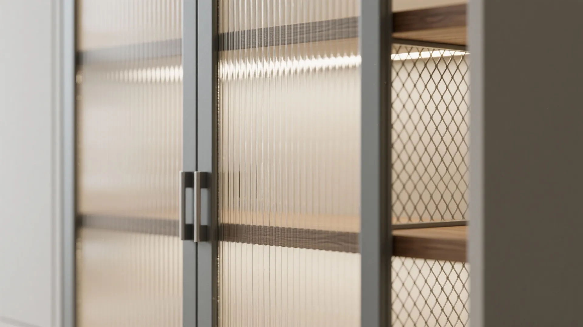 Close up of glass cabinet doors with ribbed texture and metal mesh shelving with warm lighting