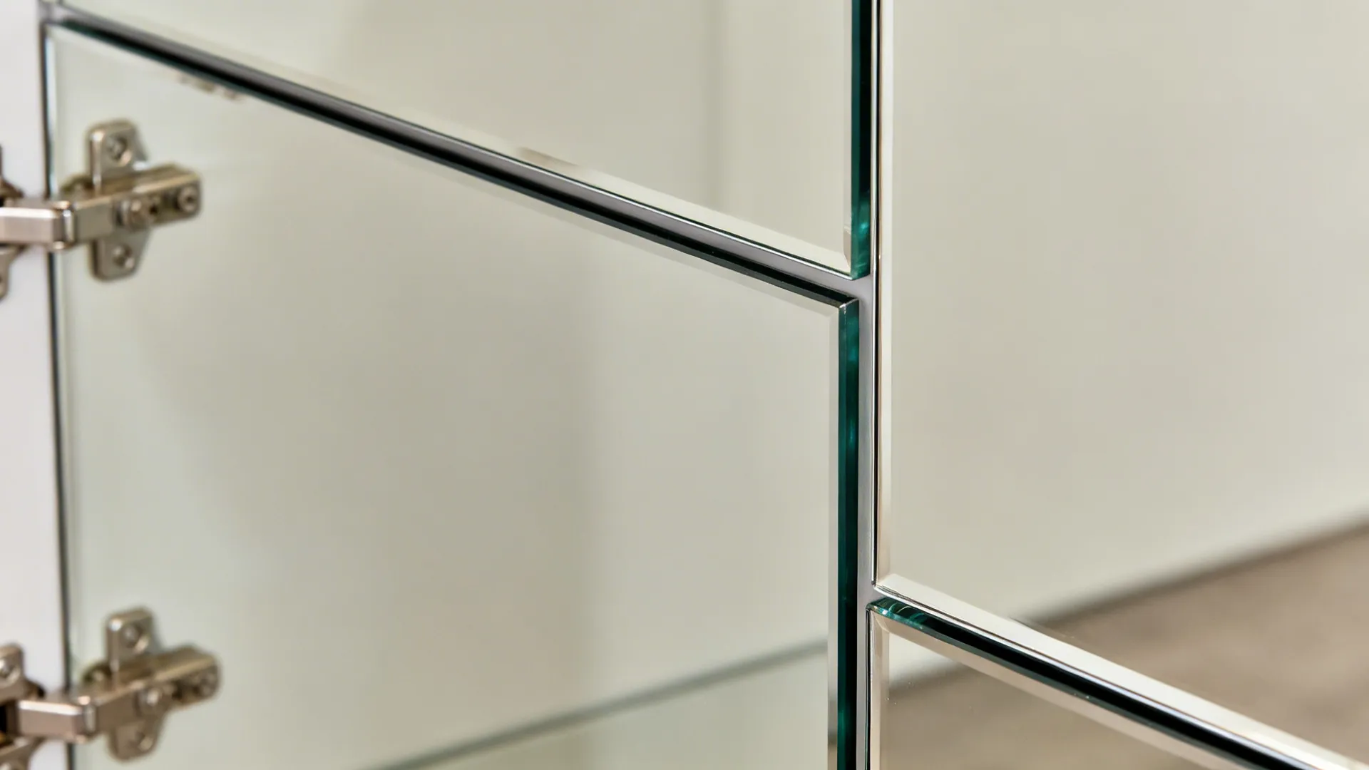 Close-up of a glass cabinet door edge and satin mirror back with soft reflections.