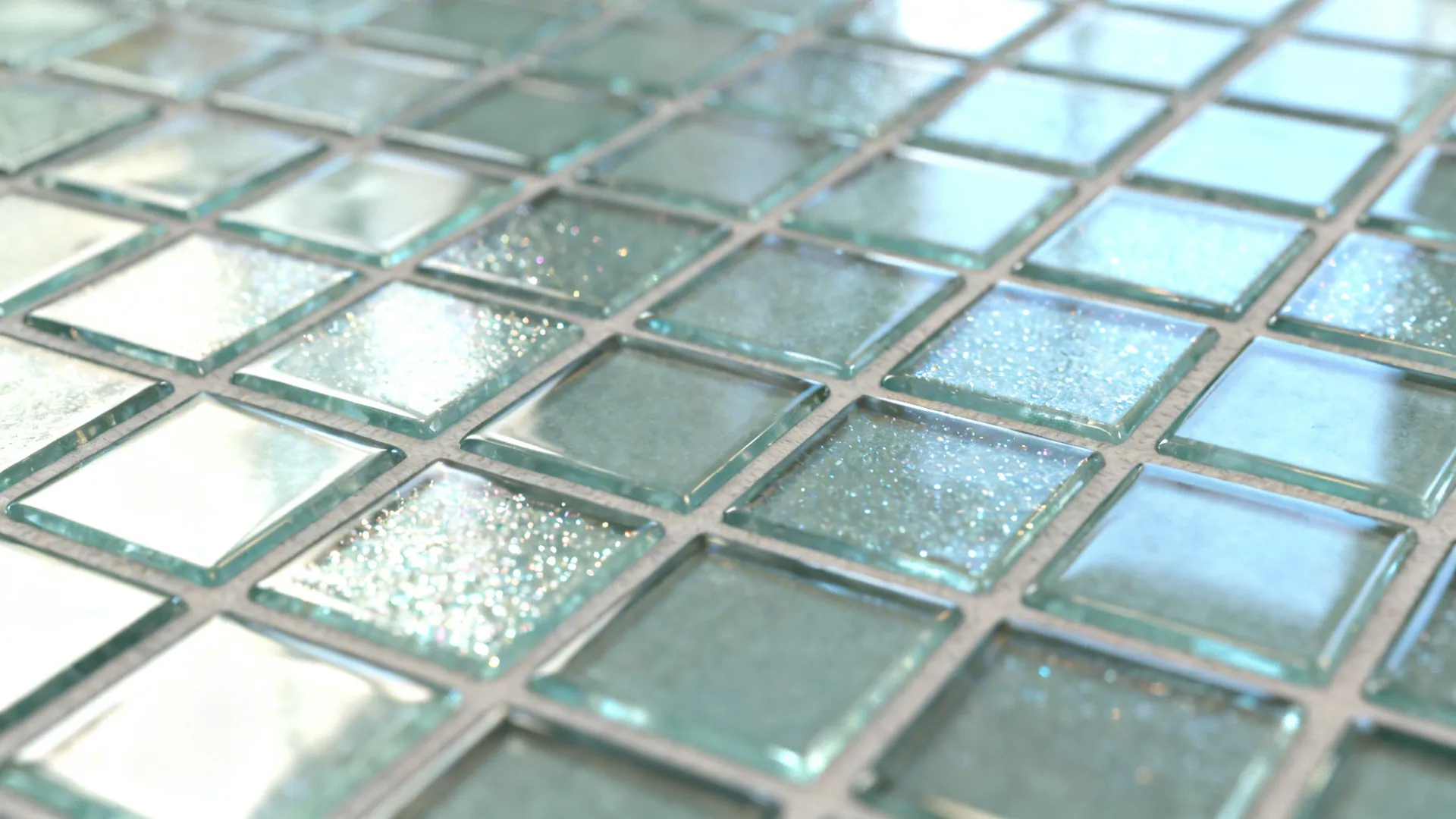 Macro of reflective glass mosaic tiles with clean grout near a sink.
