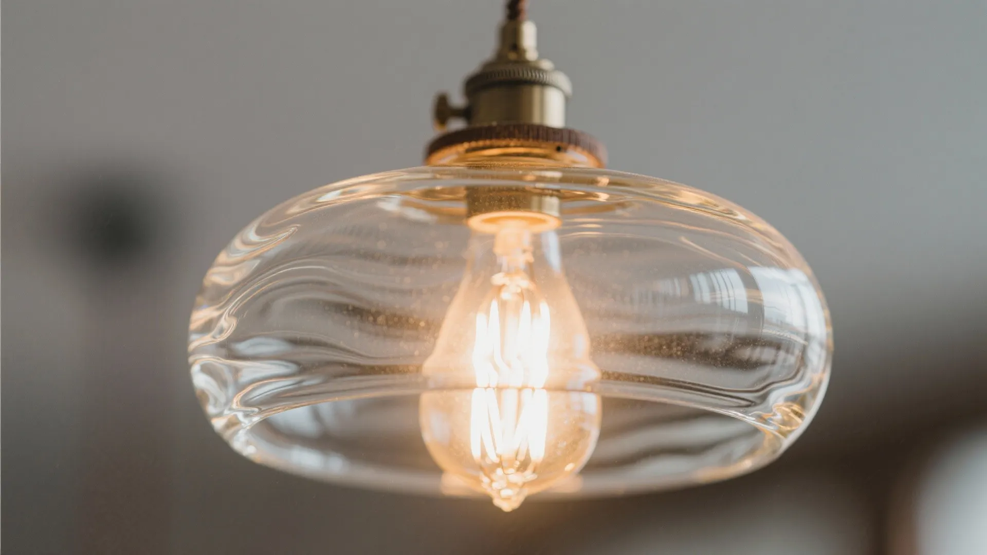 Glass ceiling light with a warm bulb inside showing a textured clear shade and brass