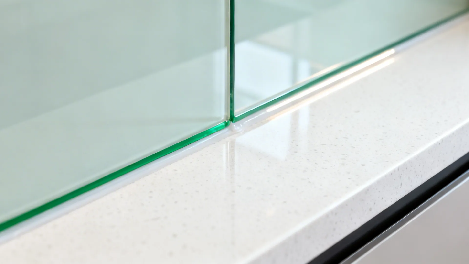 Macro of back-painted glass backsplash meeting quartz with a clean silicone seam.