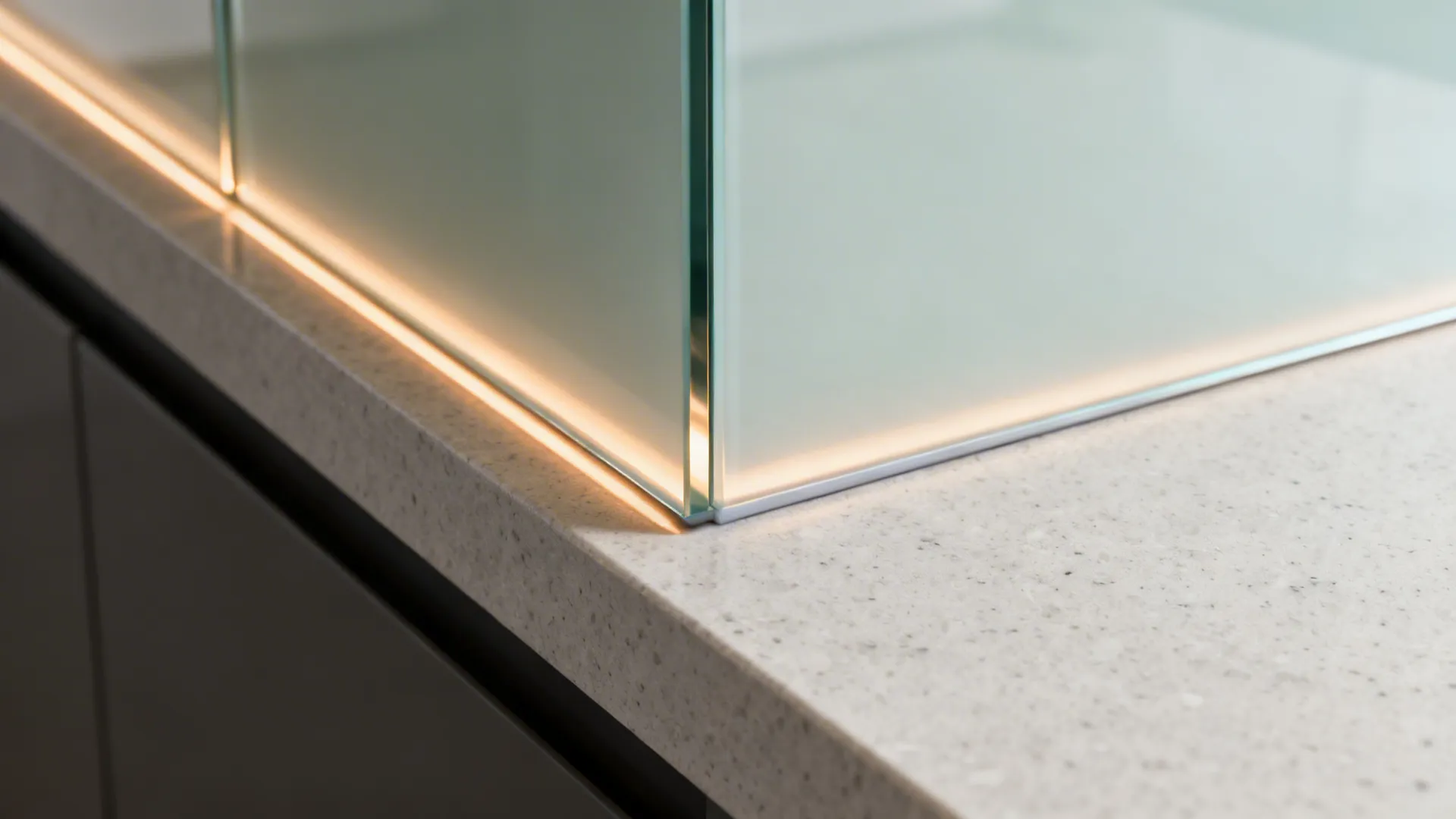Close up of glass panel corner on stone countertop with warm light strip glowing underneath detail