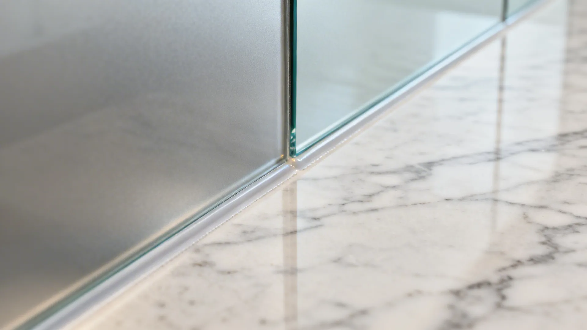 Close up of a glass panel meeting a white marble countertop with a clean joint