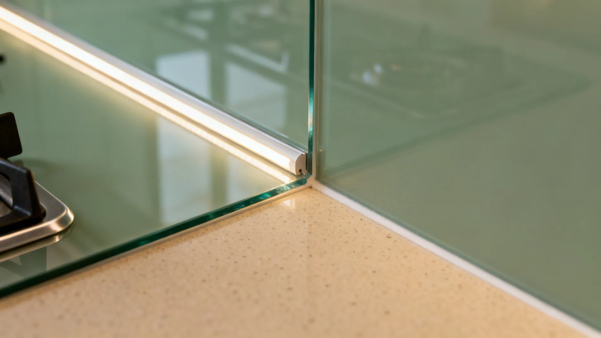 Macro of sage glass backsplash meeting beige quartz with warm task lighting.
