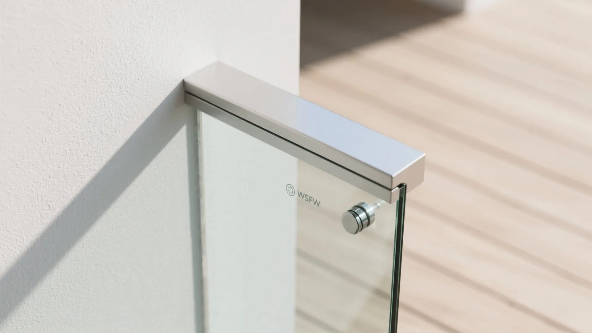 Close up view of modern glass balcony railing with metal handrail and white wall connection