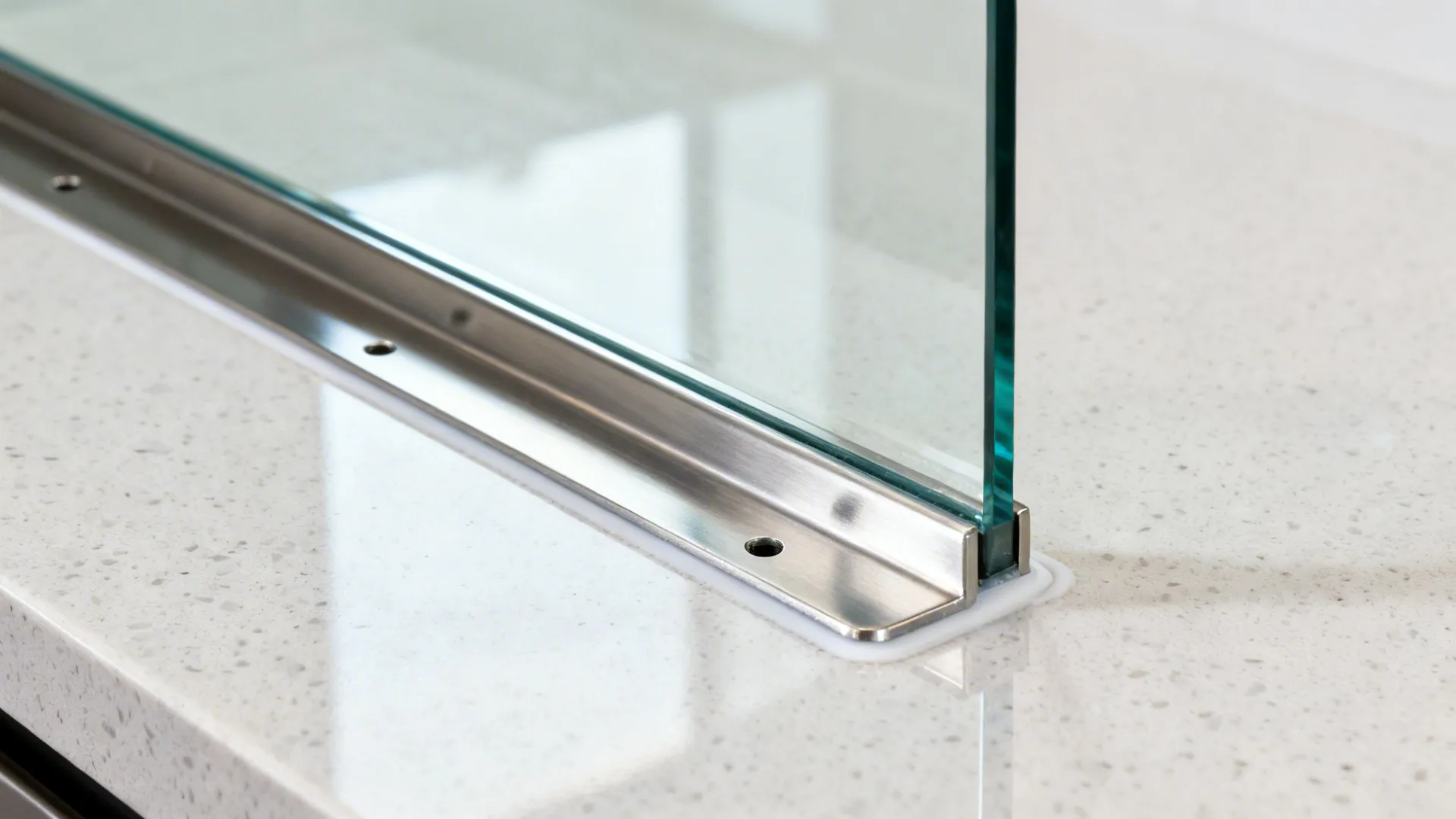 Macro of low-iron glass backsplash with stainless rail bracket and clean joint.