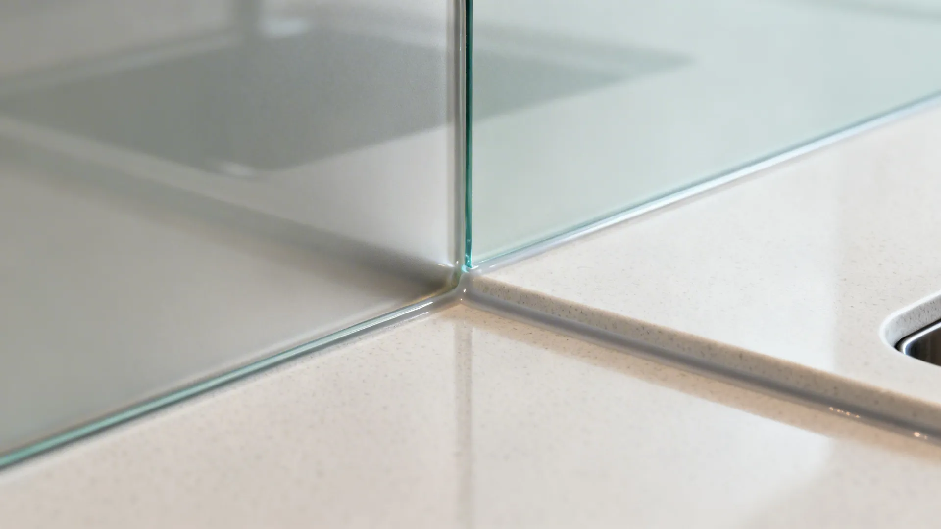 Close up view of glass panel meeting a white stone countertop with clean sealed joint