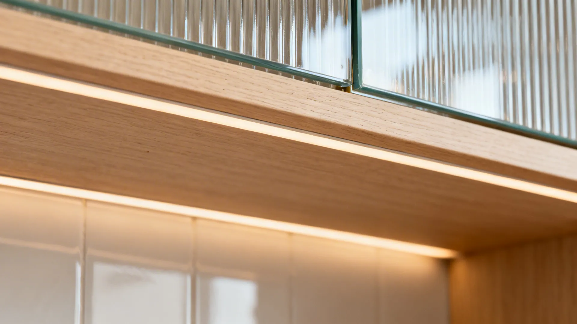 Close-up of ribbed glass door and glossy backsplash with warm LED light grazing the textures.