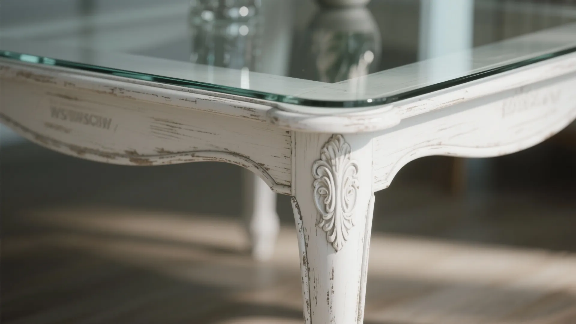 Close up of white wooden table with glass top showing ornate leg and carved design