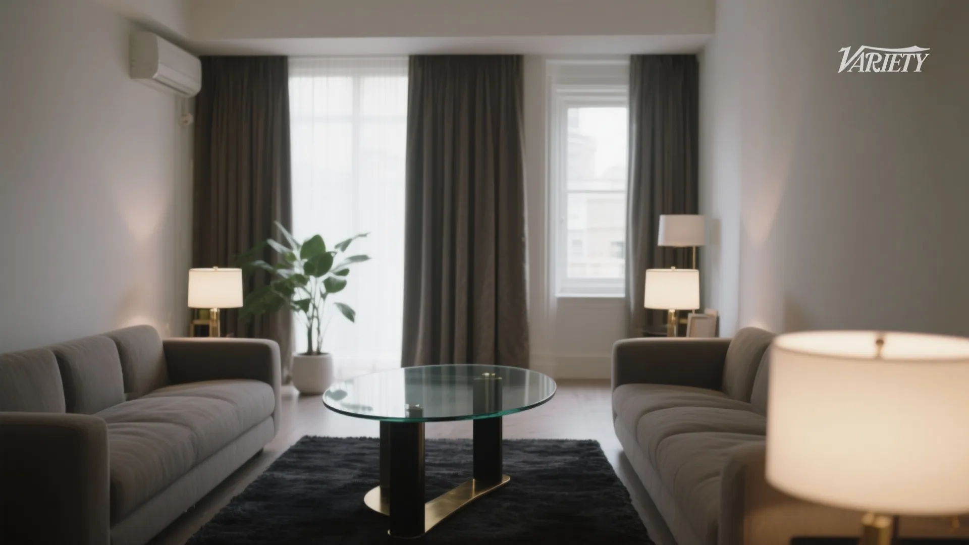 Modern living room with grey sofas glass coffee table dark rug and warm table light