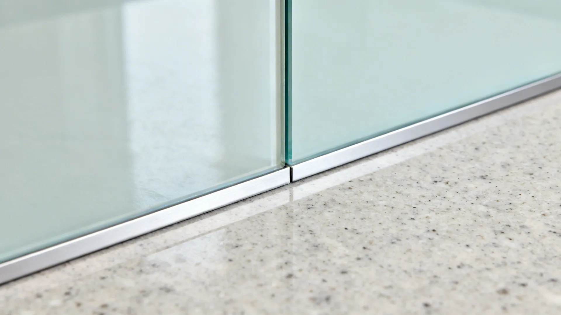 Macro of low-iron glass backsplash with slim aluminum trim above a quartz countertop.