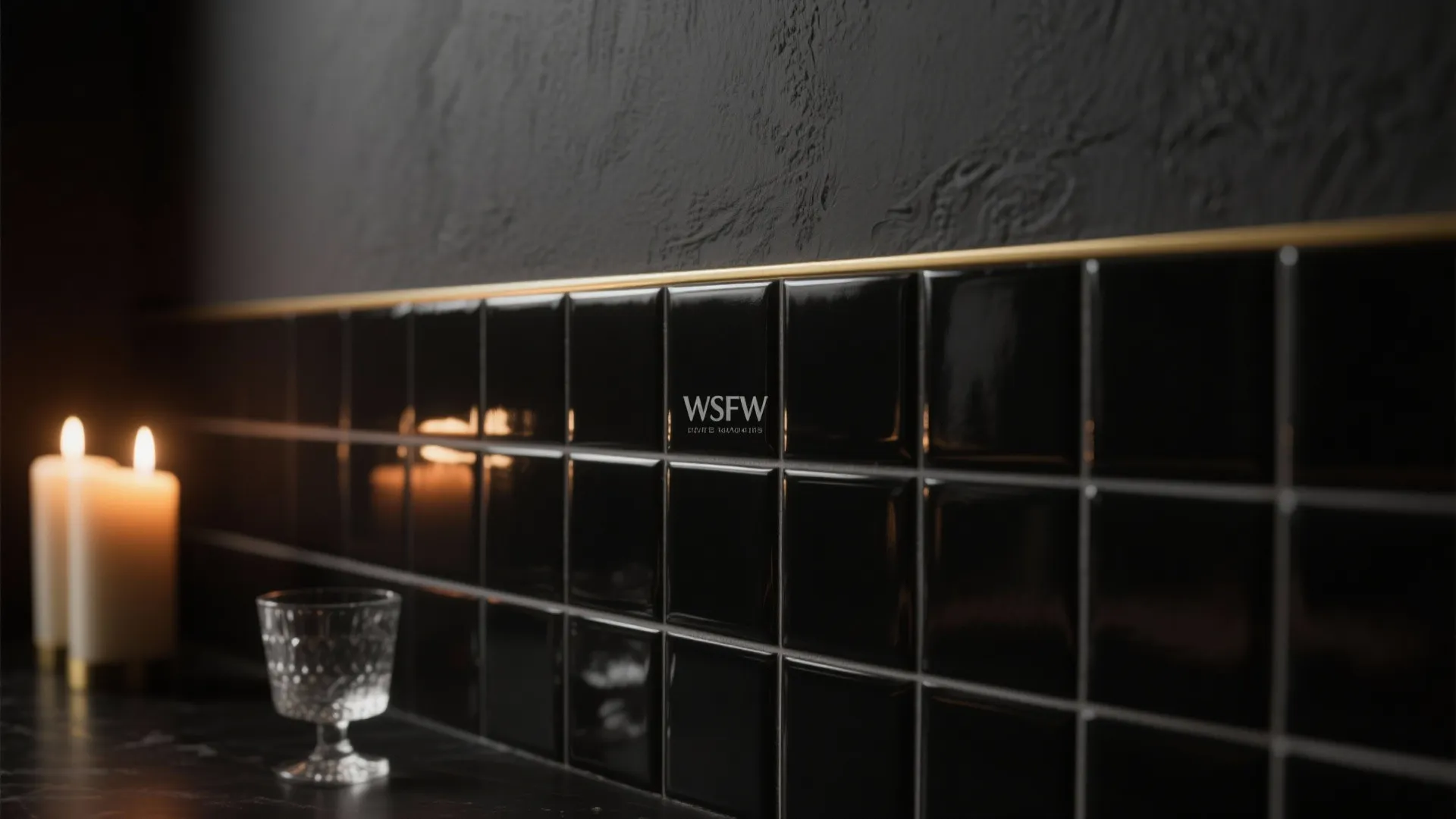 Glossy black wall tiles with gold trim strip next to burning candles and glass cup