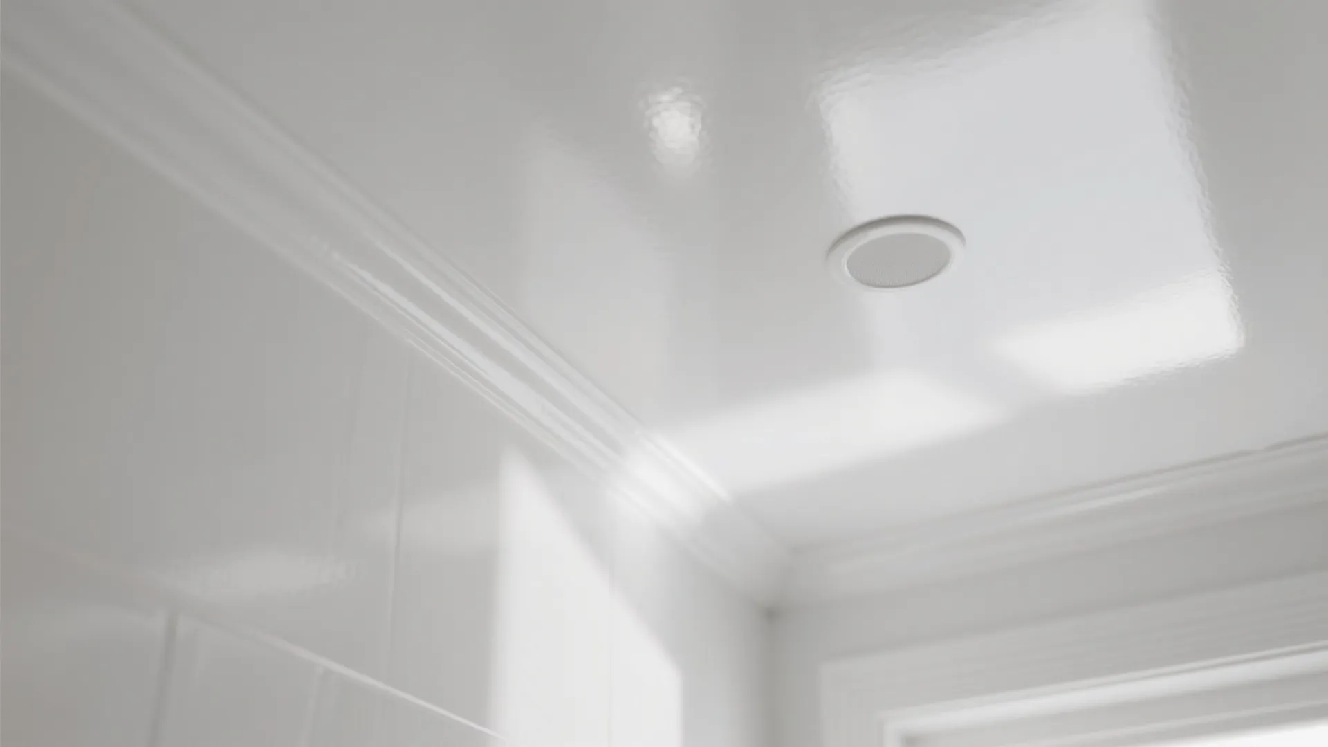 Close up view of a glossy white ceiling with crown molding and small recessed light