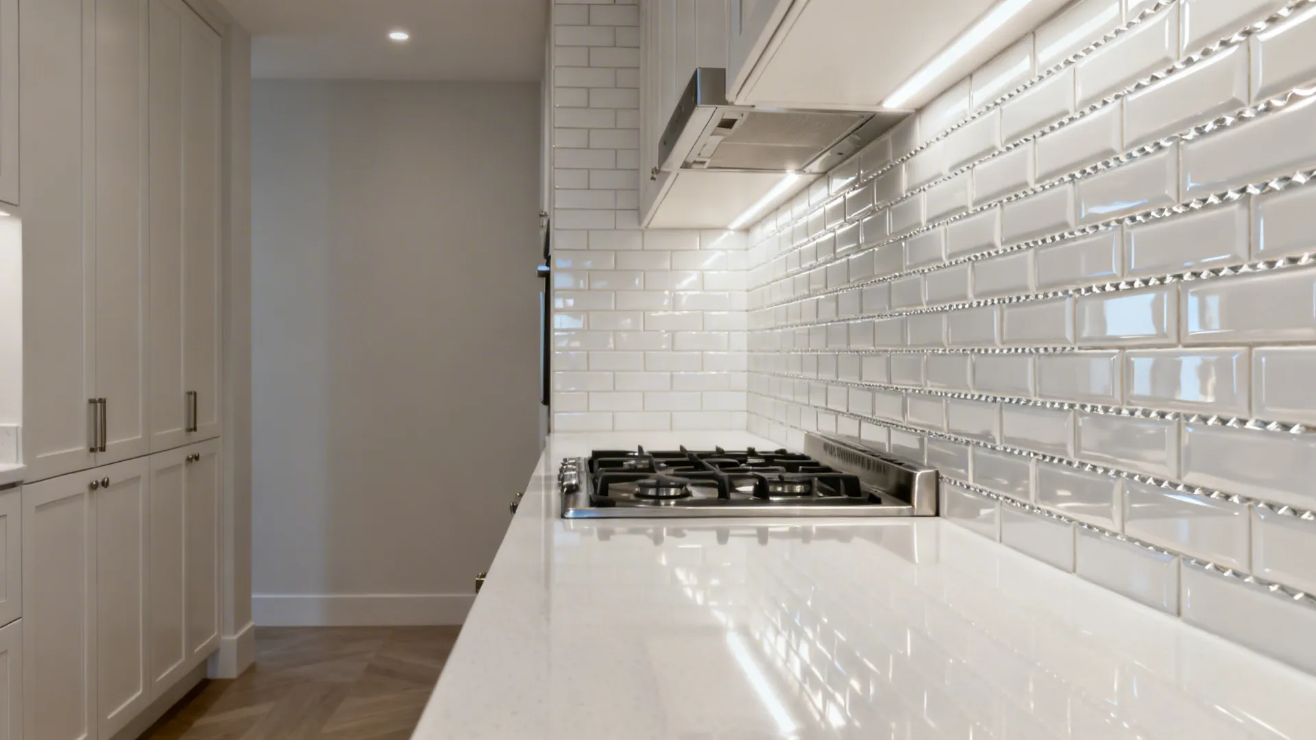 High-gloss white subway tile backsplash in a narrow galley kitchen reflecting soft daylight.