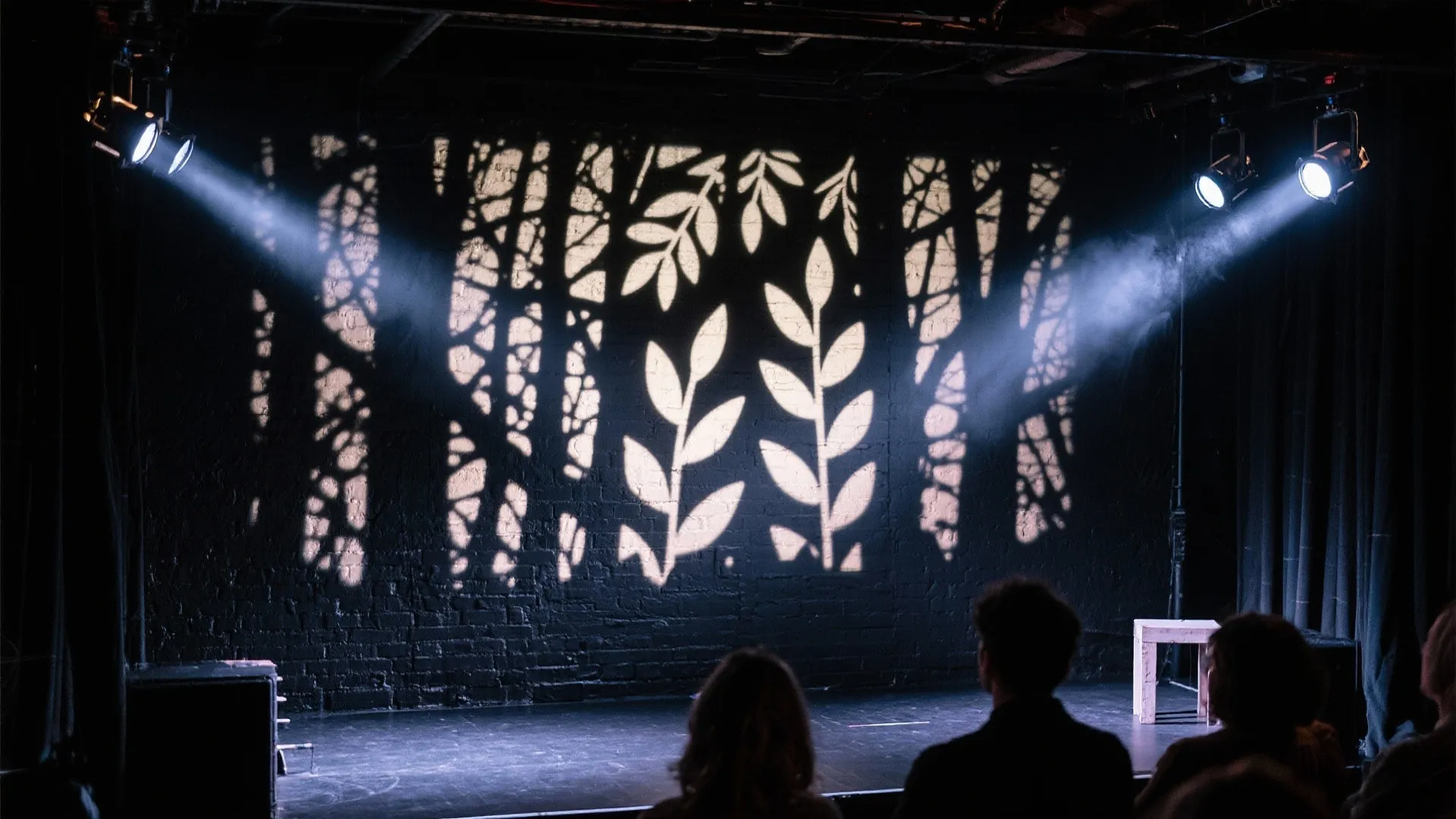 Dark stage with leaf shadows projected on a brick wall using bright spotlights and audience members
