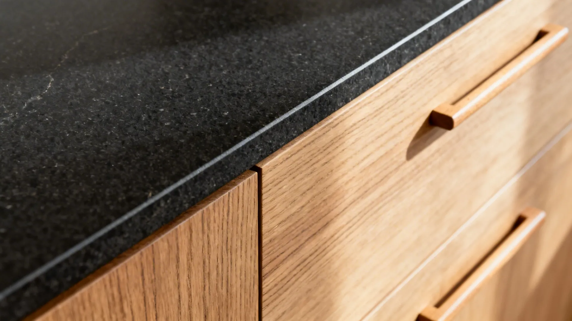 Macro of honed black granite edge meeting rift-cut oak drawer with slim pull