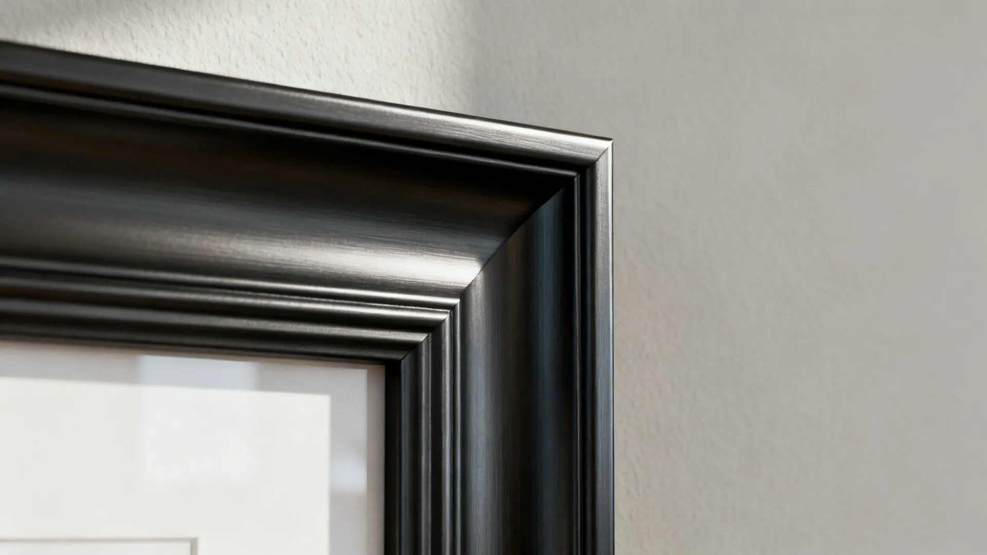 Macro of a satin black picture frame edge set against a light greige wall.