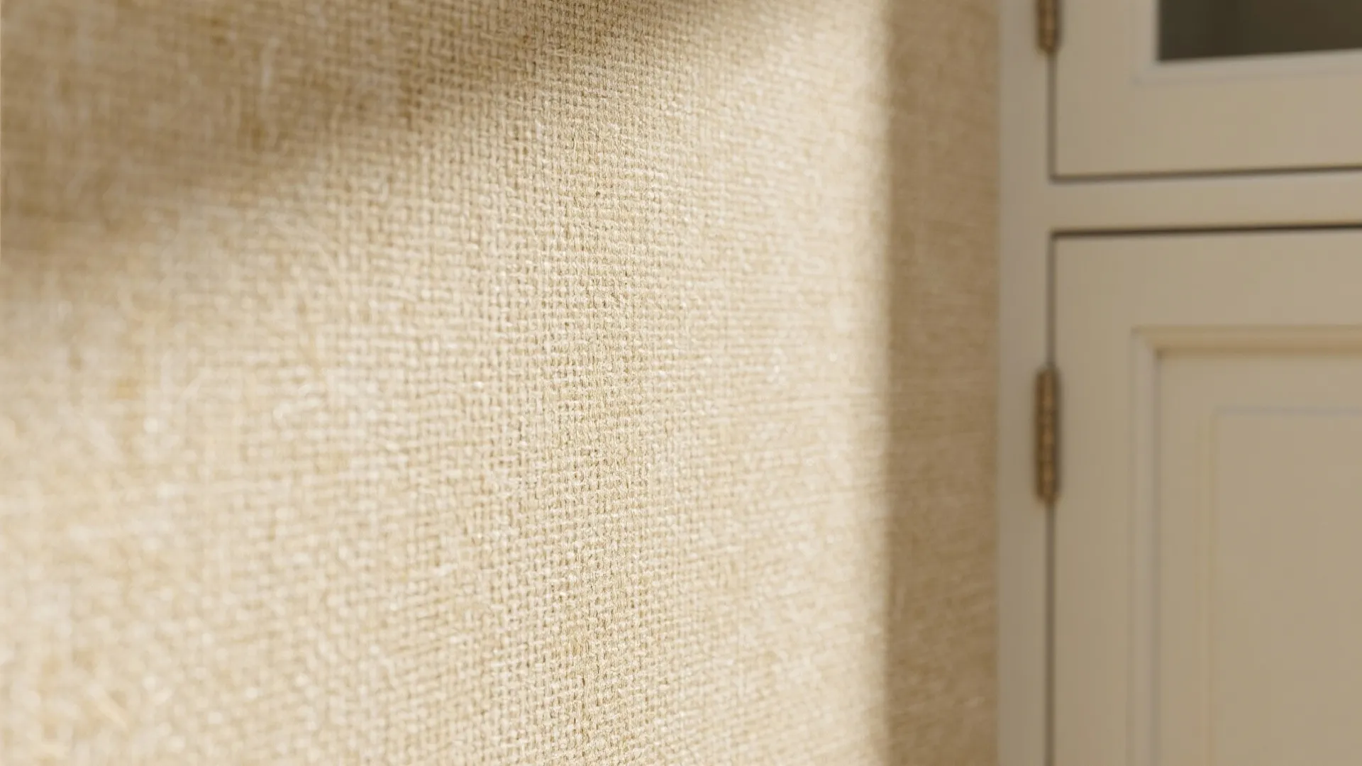 Close up of beige textured woven wallpaper on a room wall next to white cabinet