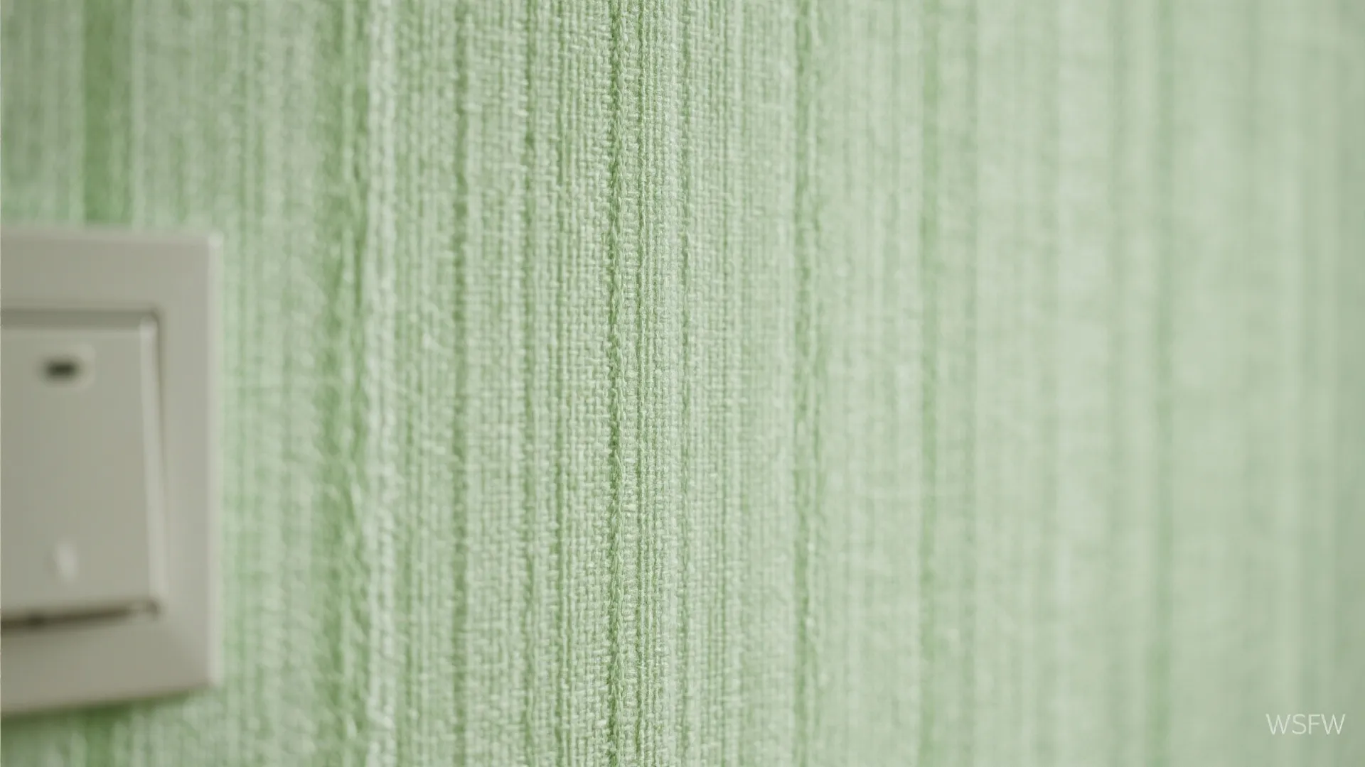 Macro view of green textured wallpaper with vertical lines next to a white light wall switch