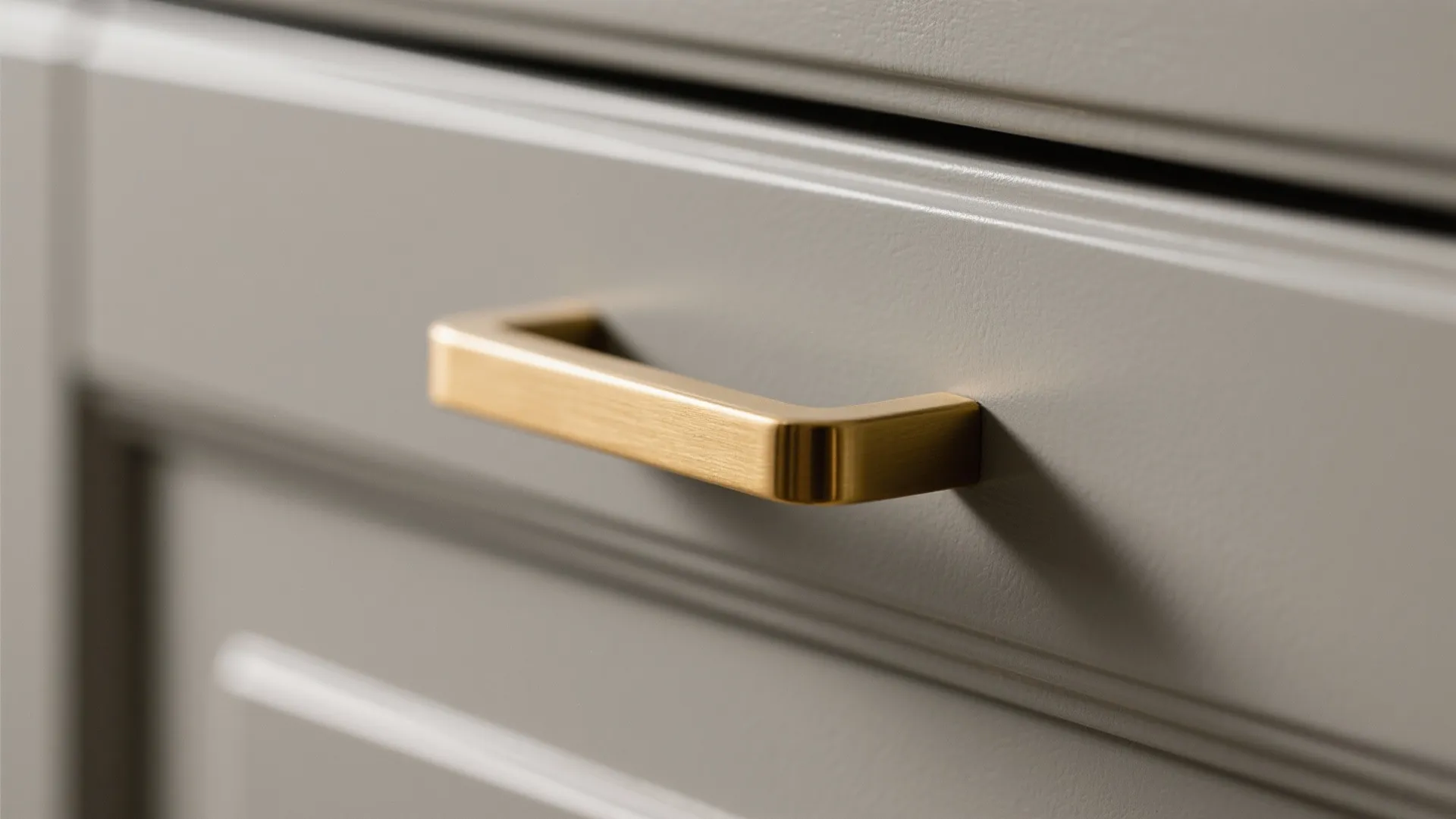 Close up of a gold metal handle attached to a grey kitchen cabinet drawer front surface