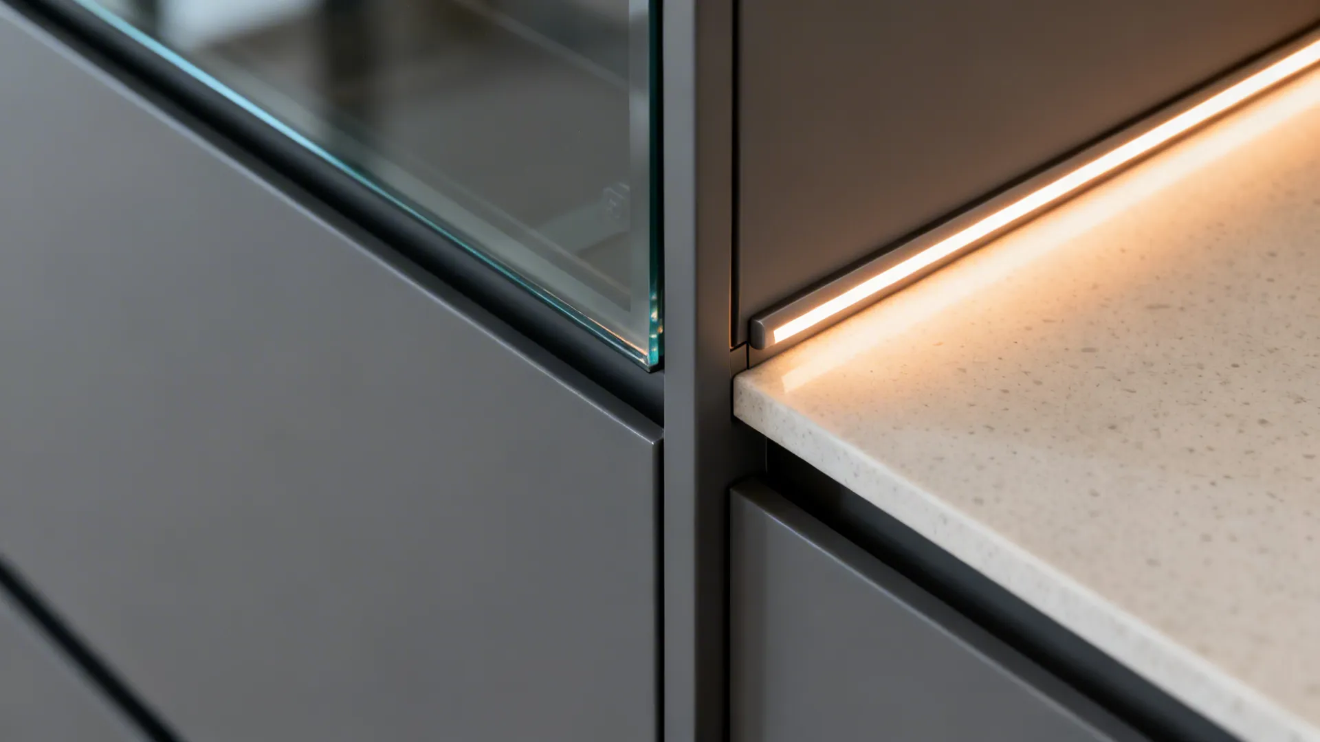 Dark grey kitchen cabinet detail with a warm light strip under a white stone countertop