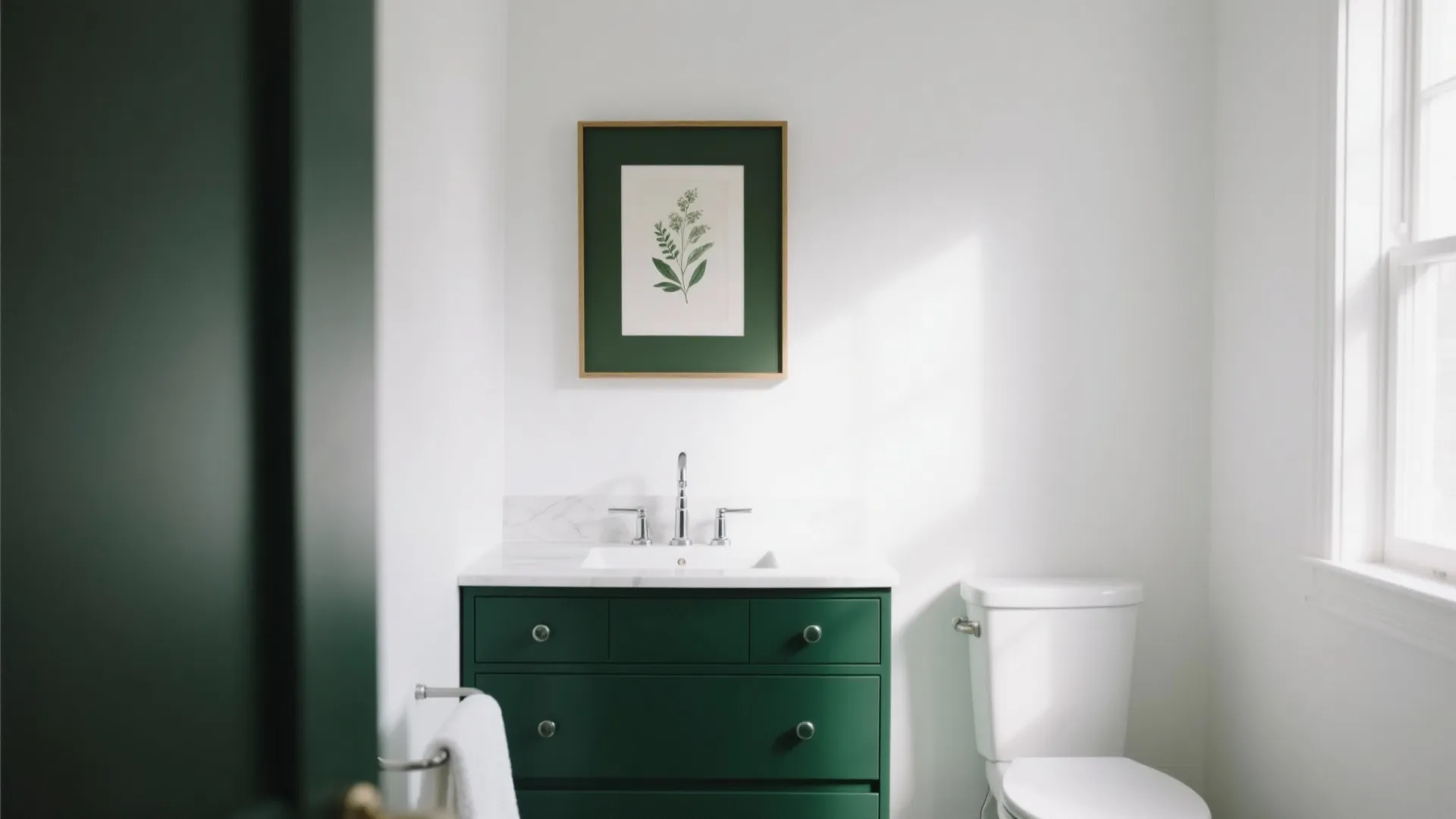 Bright white bathroom featuring green cabinet white toilet plant wall art and natural window light