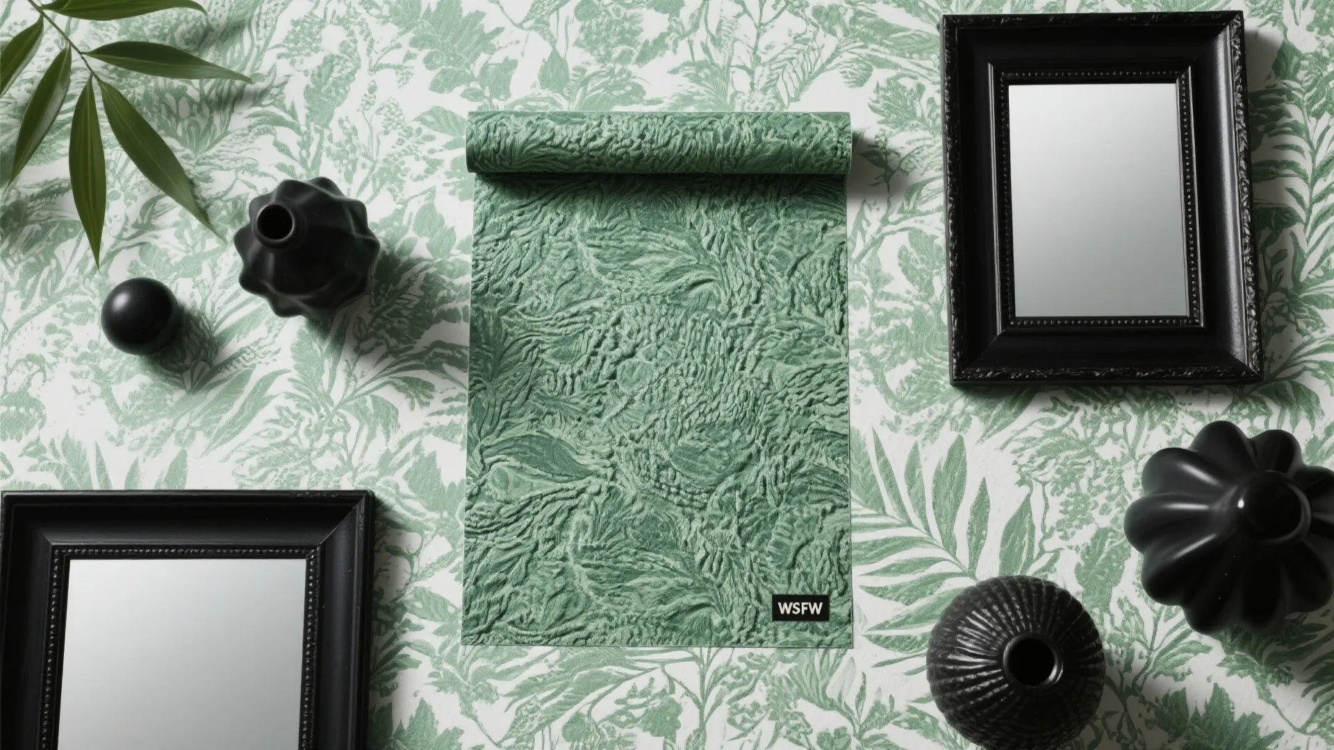 Green patterned wallpaper with textured fabric sample black picture frames and small black decorative vases